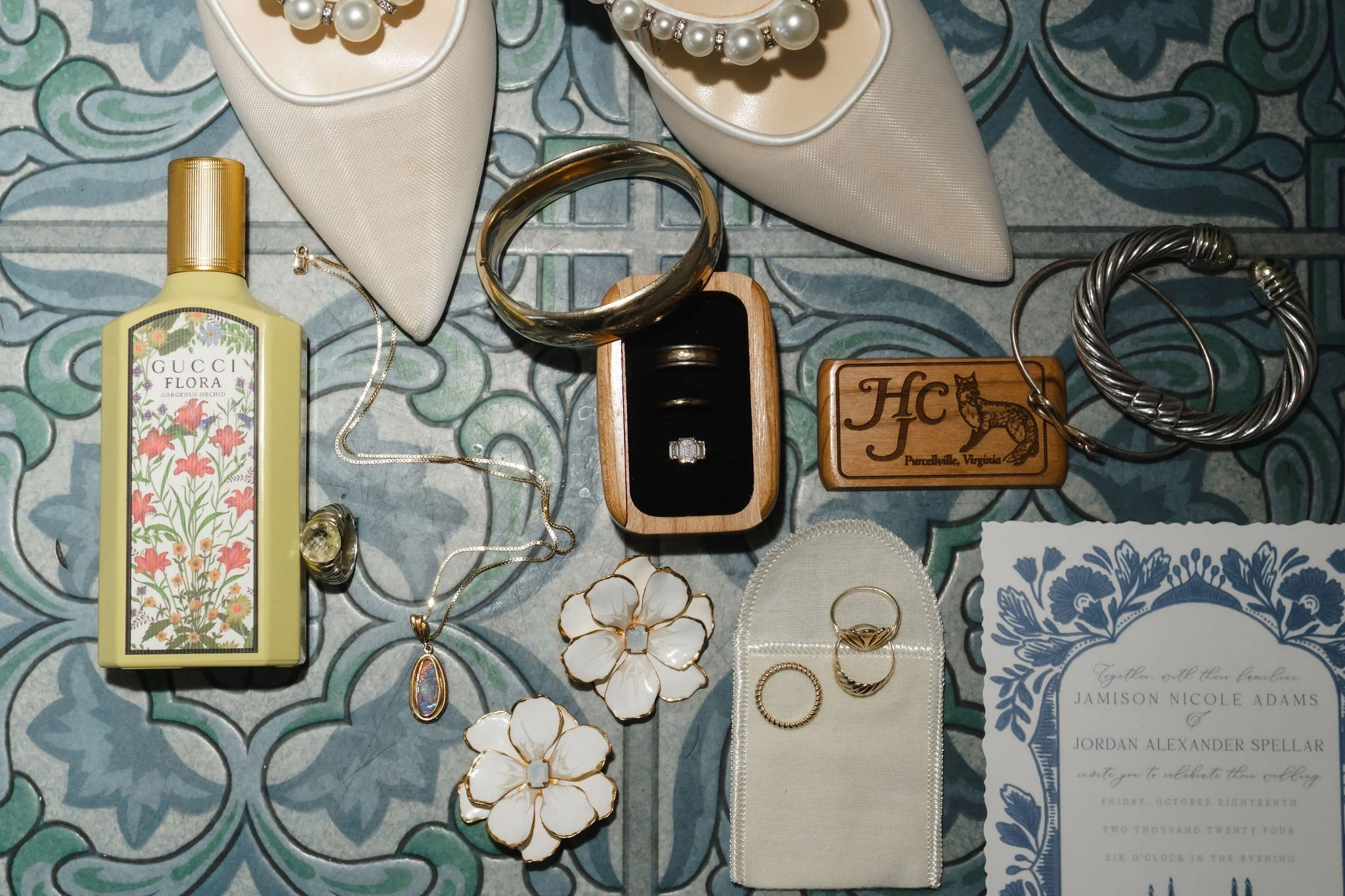 Collection of jewelry and accessories including two white floral earrings with gold edges, a gold ring, a pair of silver hoop earrings, a ring with a clear stone, a necklace with a colorful pendant, a pair of cream-colored pointed-toe shoes with pear