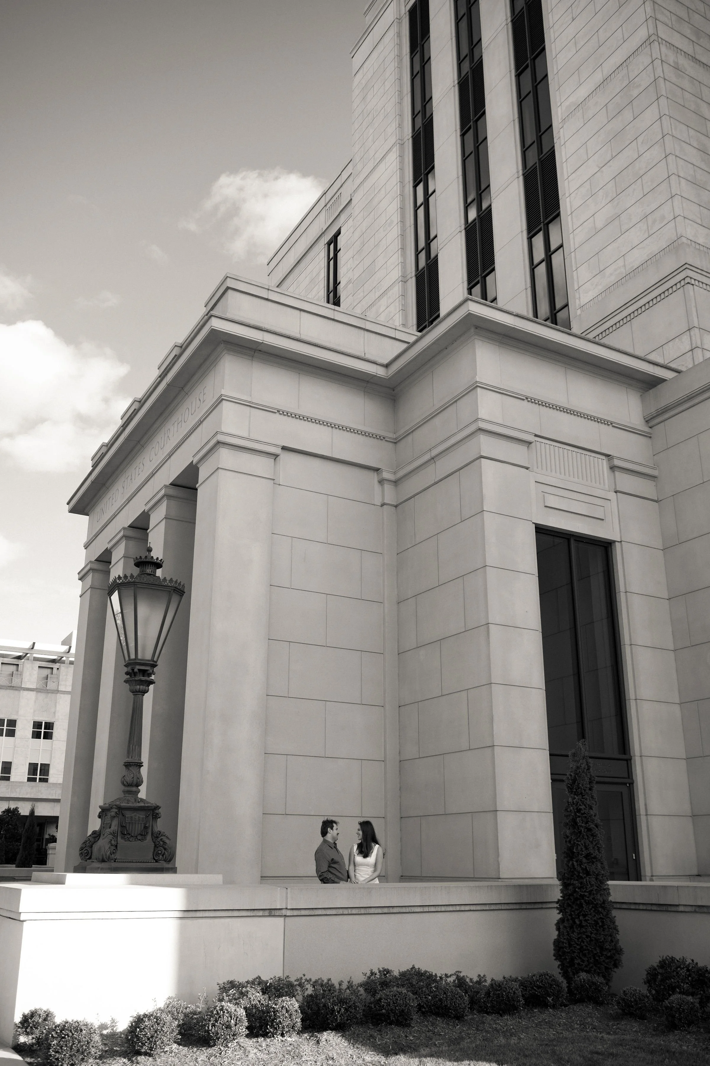 Two people standing and talking outside the United States Courthouse, a large stone building with classical architecture and tall windows.