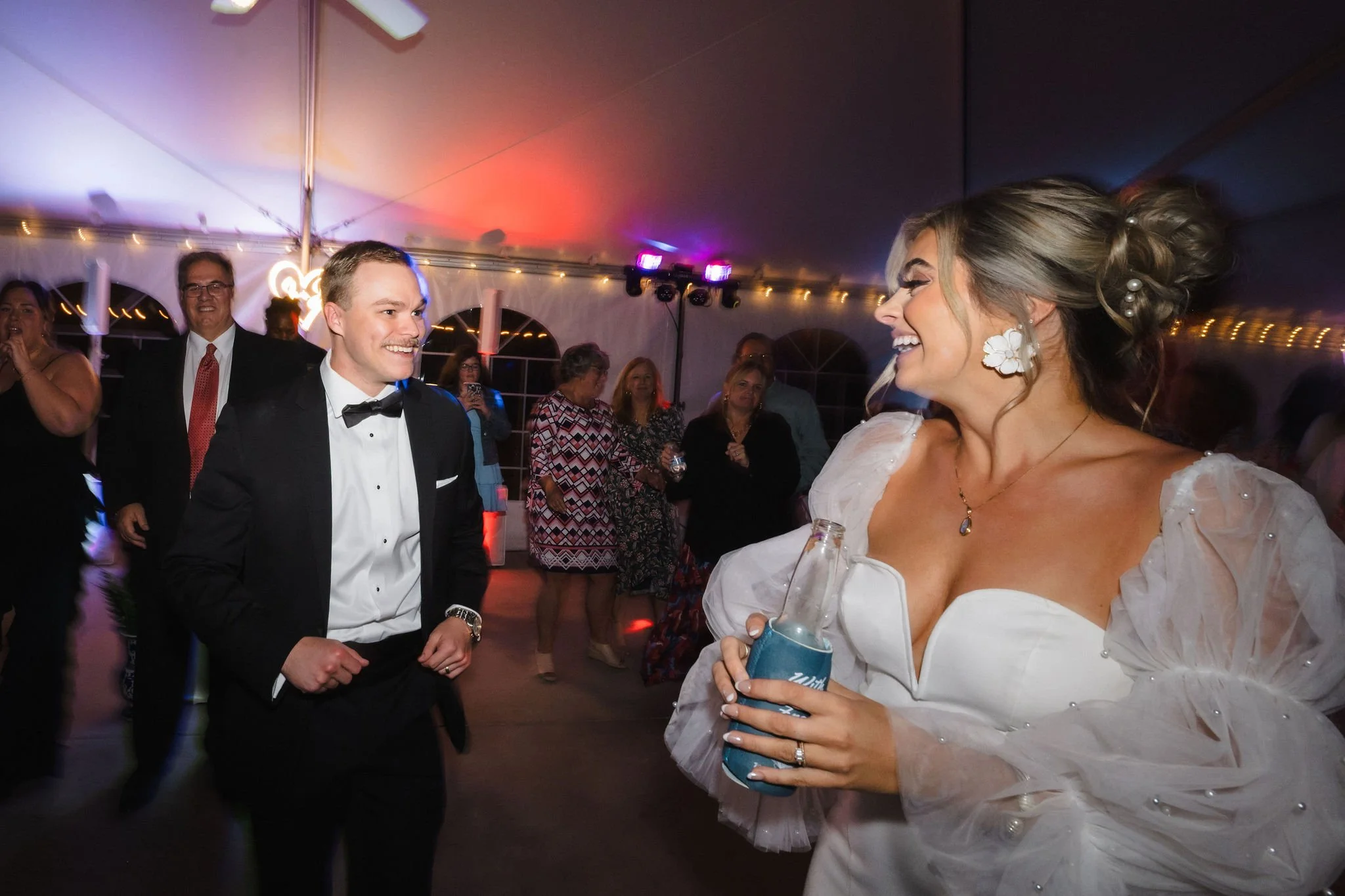 Bride and groom dancing at a wedding reception inside a decorated tent with guests in the background.