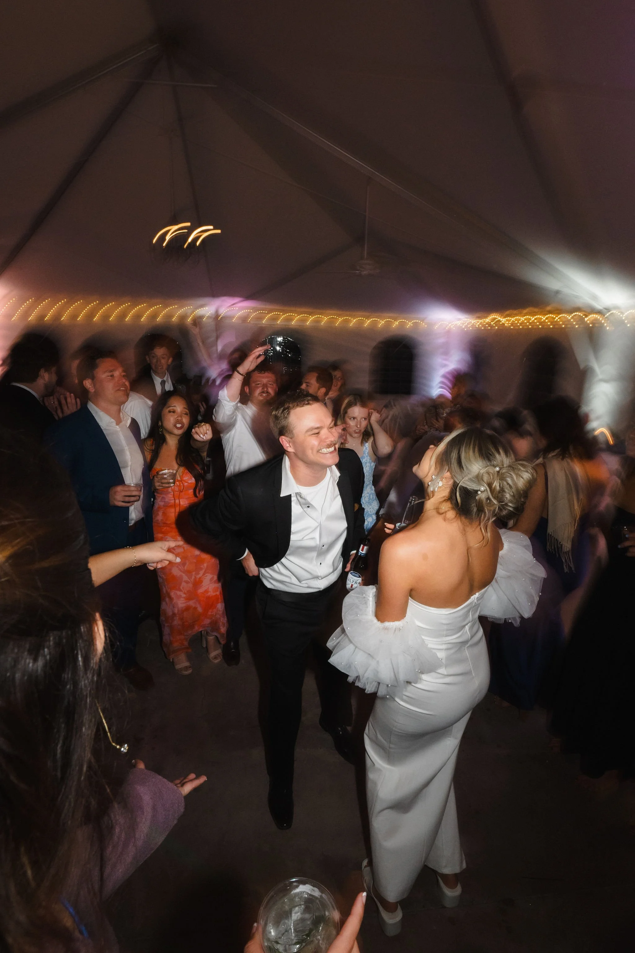 People dancing and celebrating at a lively party under a tent with string lights