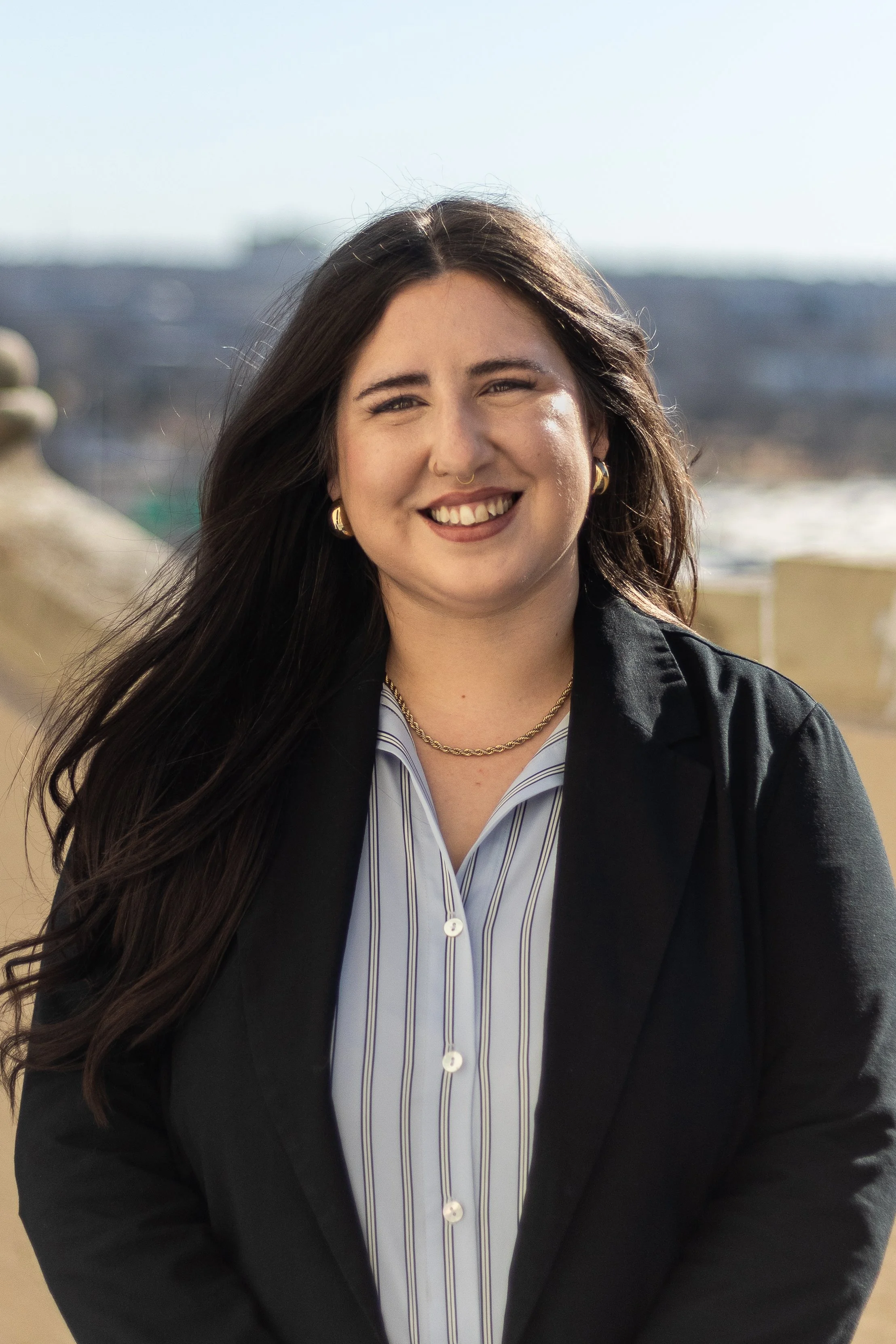 A smiling woman with shoulder-length reddish-brown hair, wearing a dark green top, standing against a plain white background.