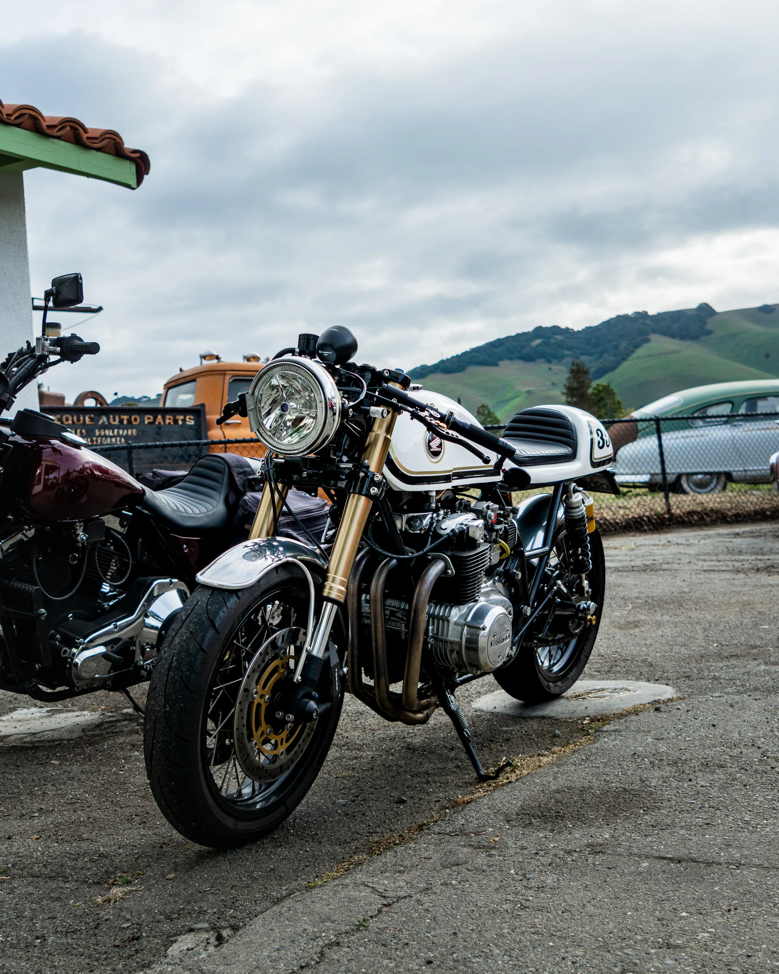 A vintage-style motorcycle parked on a parking lot with a scenic hilly landscape in the background.
