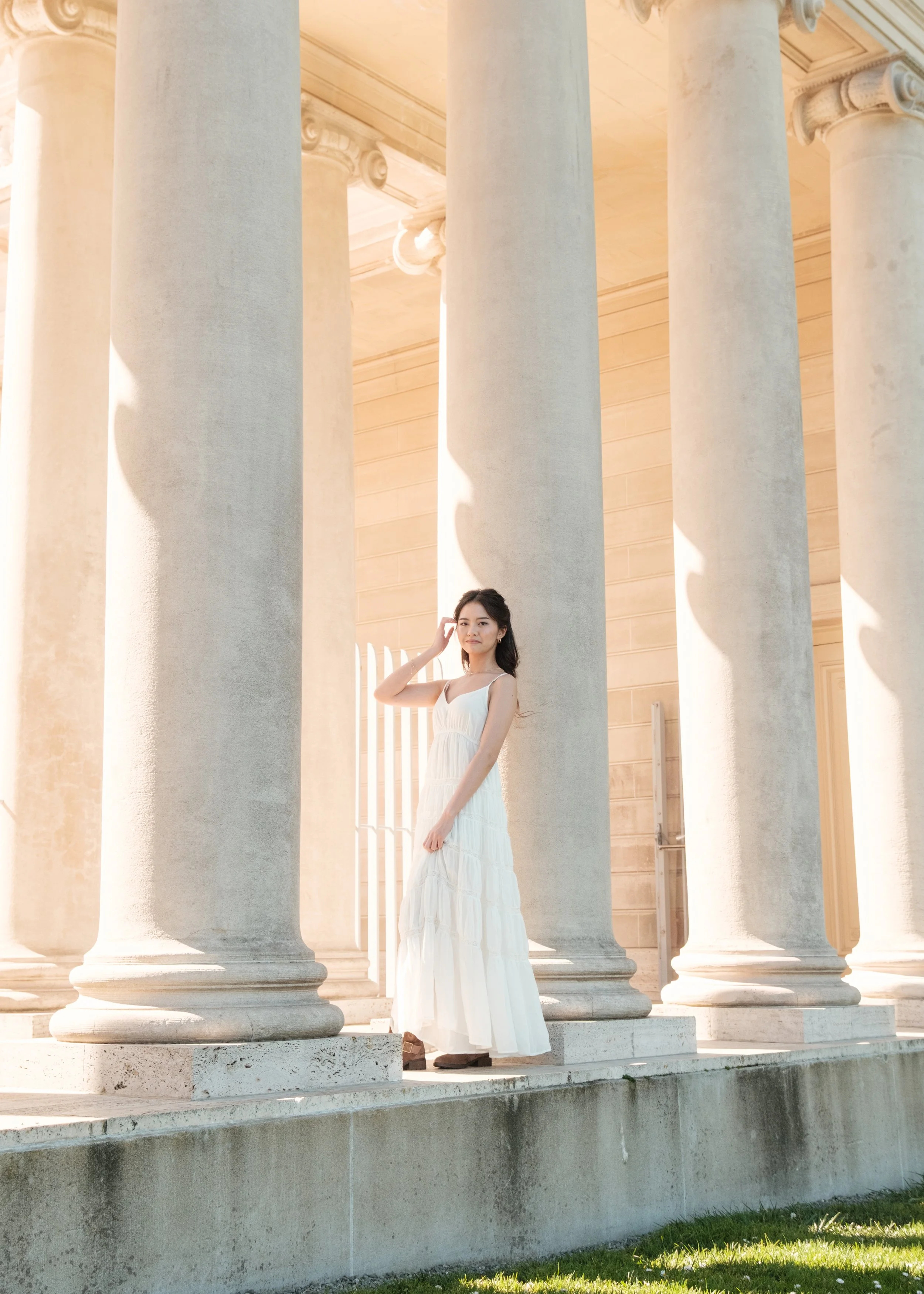 A woman in a white dress standing between large marble columns of a classical building.