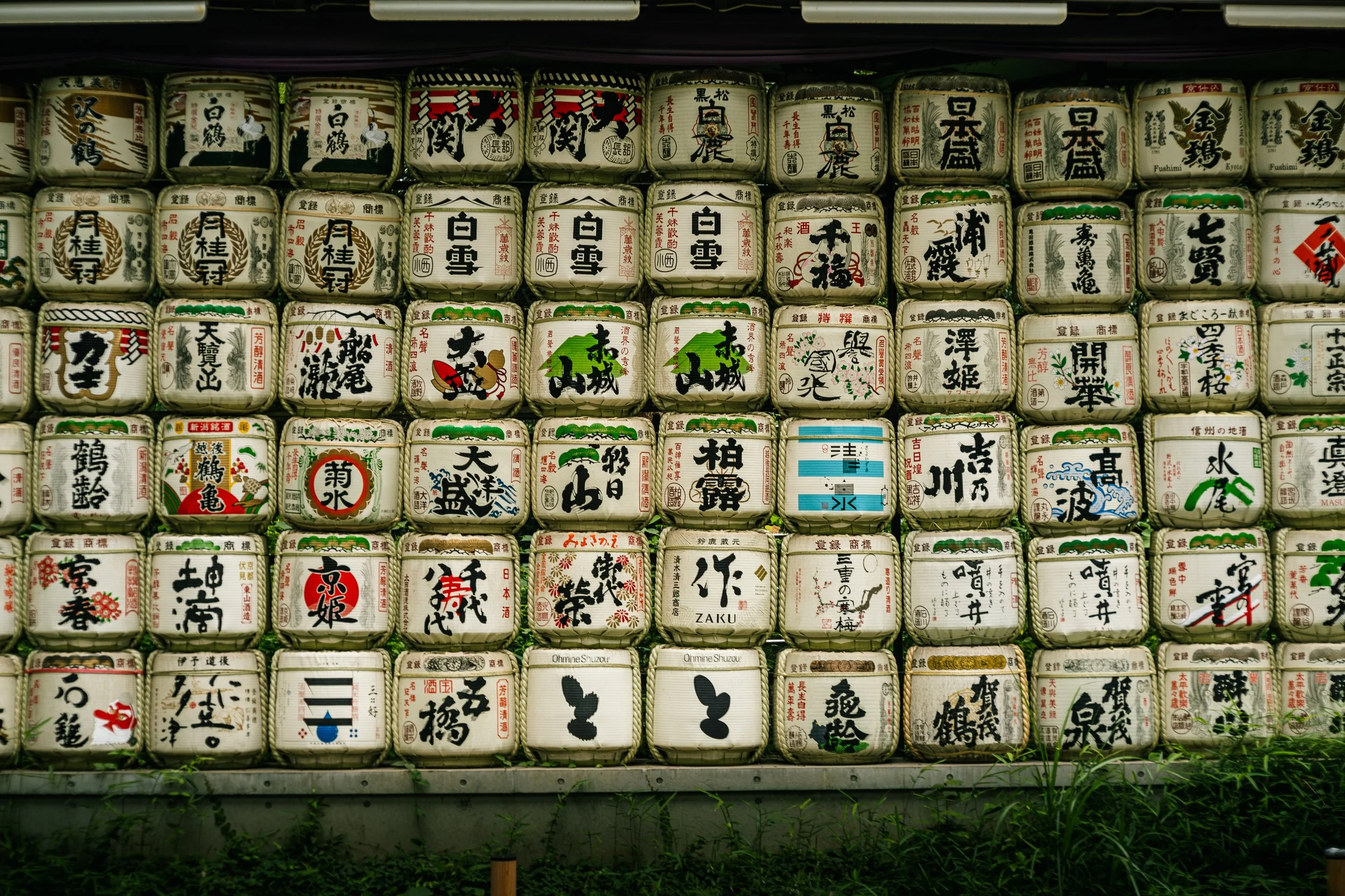 Wall of traditional Japanese sake barrels decorated with Japanese calligraphy and designs, arranged in a grid pattern.