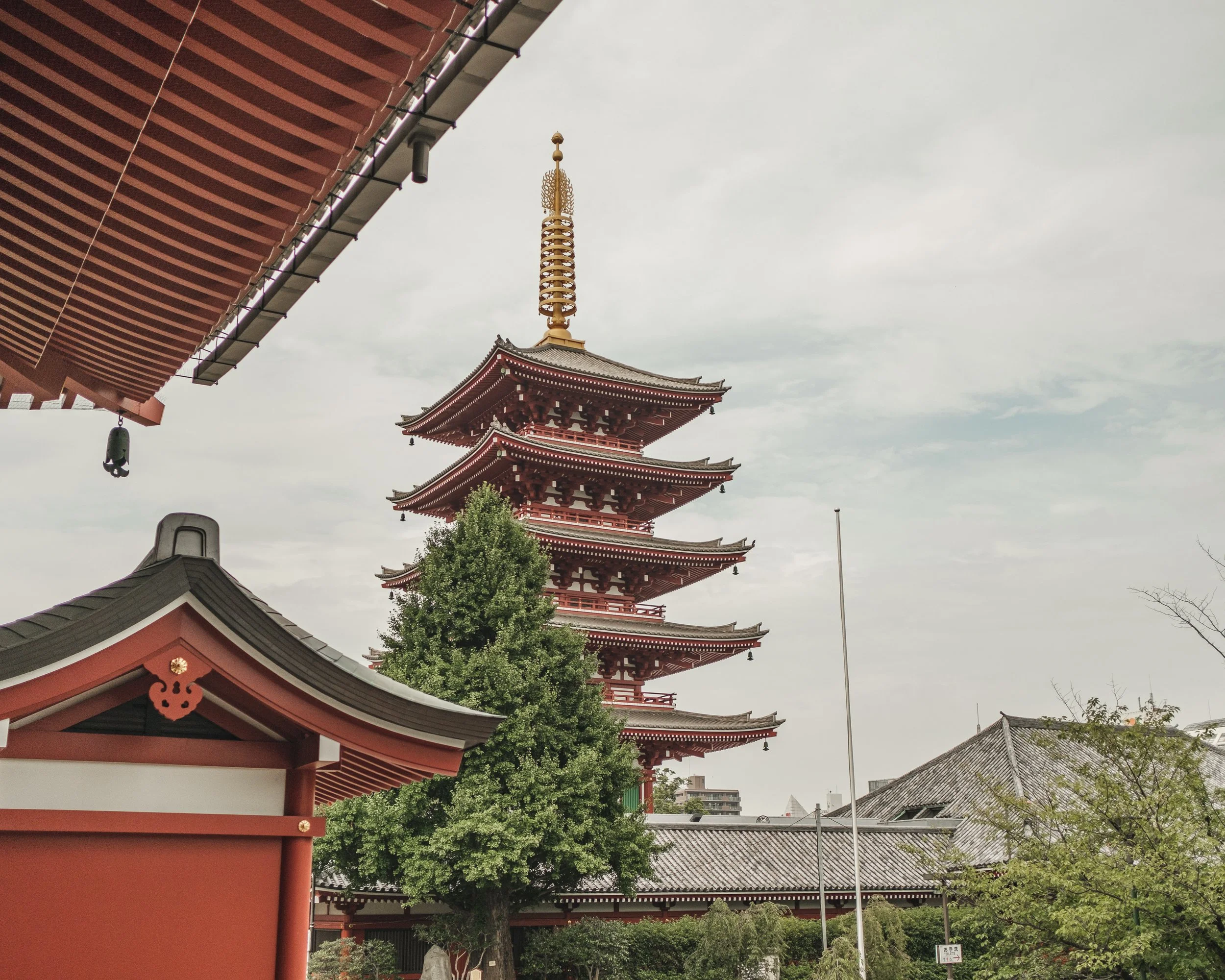 A traditional five-story Japanese pagoda with a red and white color scheme, surrounded by trees and traditional Japanese buildings, under a cloudy sky.