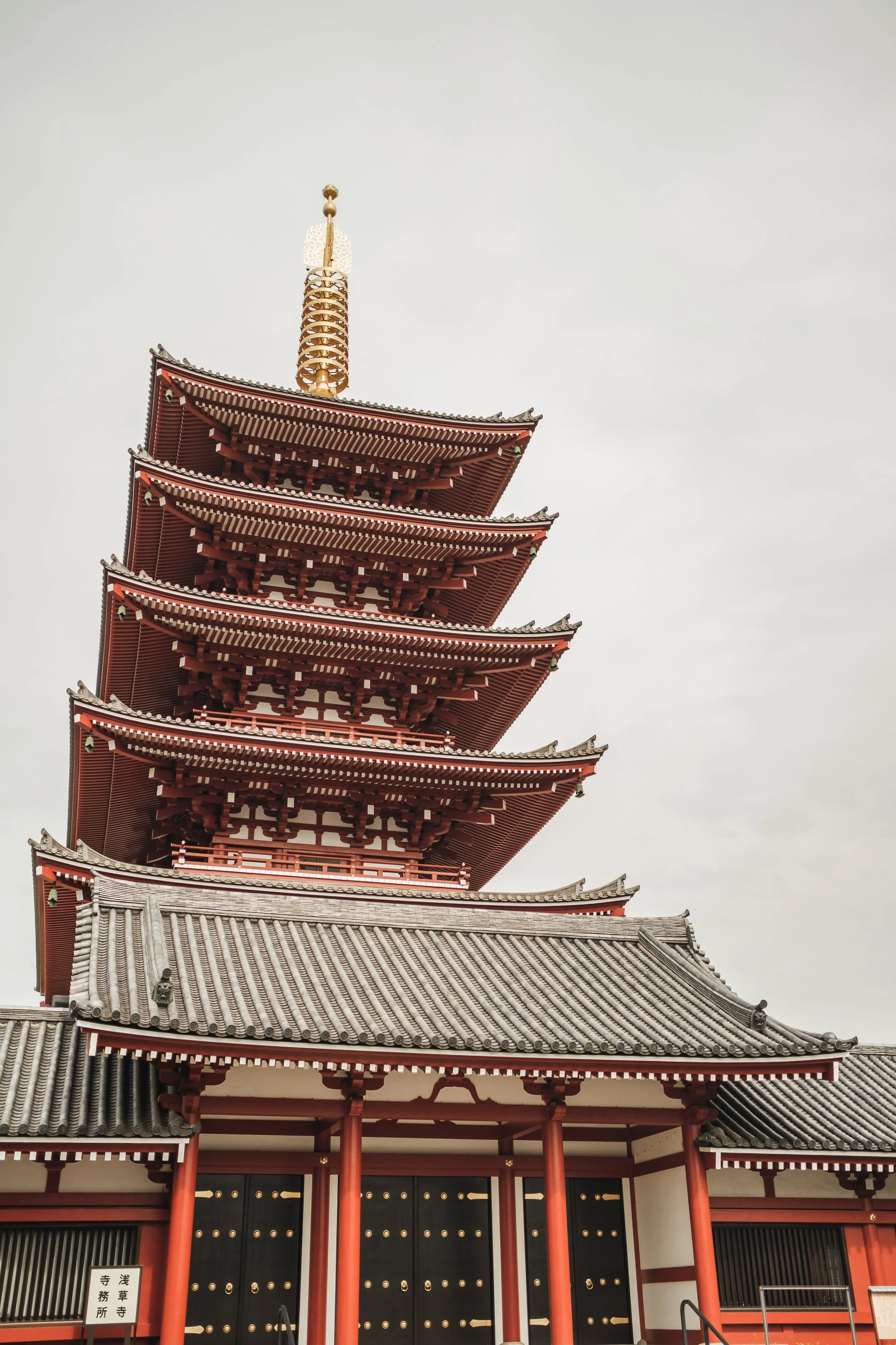 A five-tier traditional Japanese pagoda with a red and black structure and gray tiled roofs, set against an overcast sky.