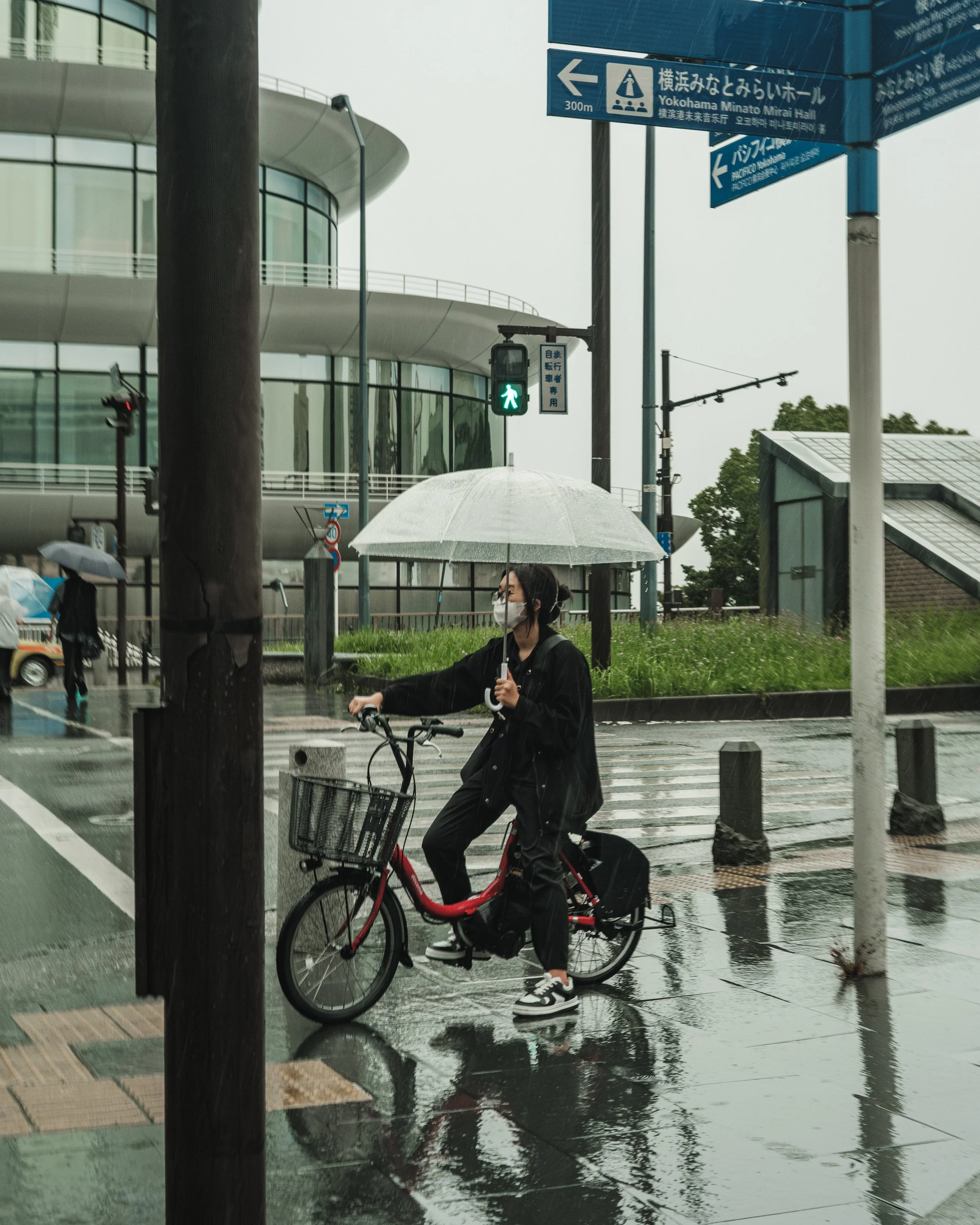 Person wearing a mask holding an umbrella while riding a bicycle on rainy day at crosswalk