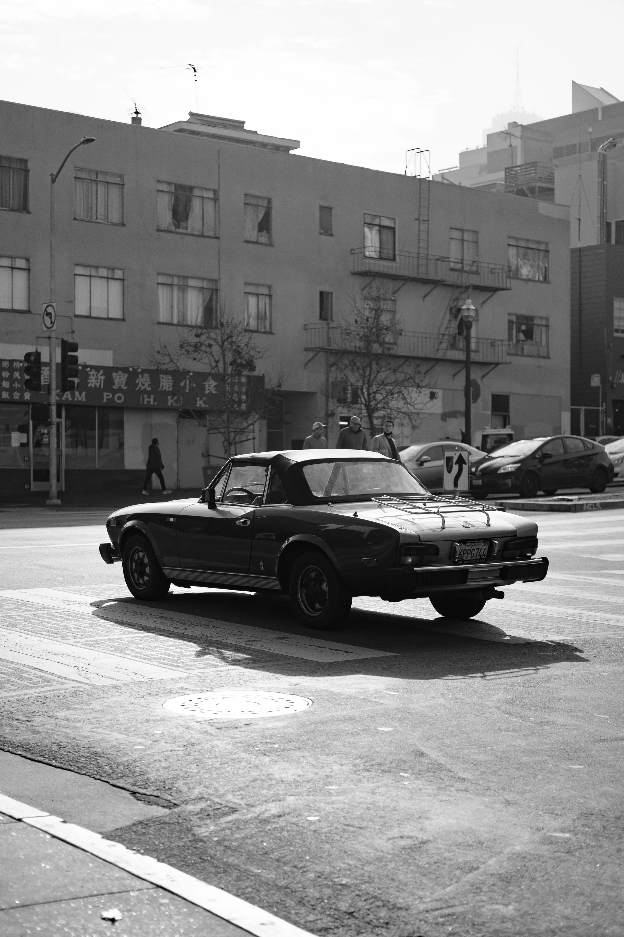 Black vintage convertible car stopped at a crosswalk on an urban street in black and white.