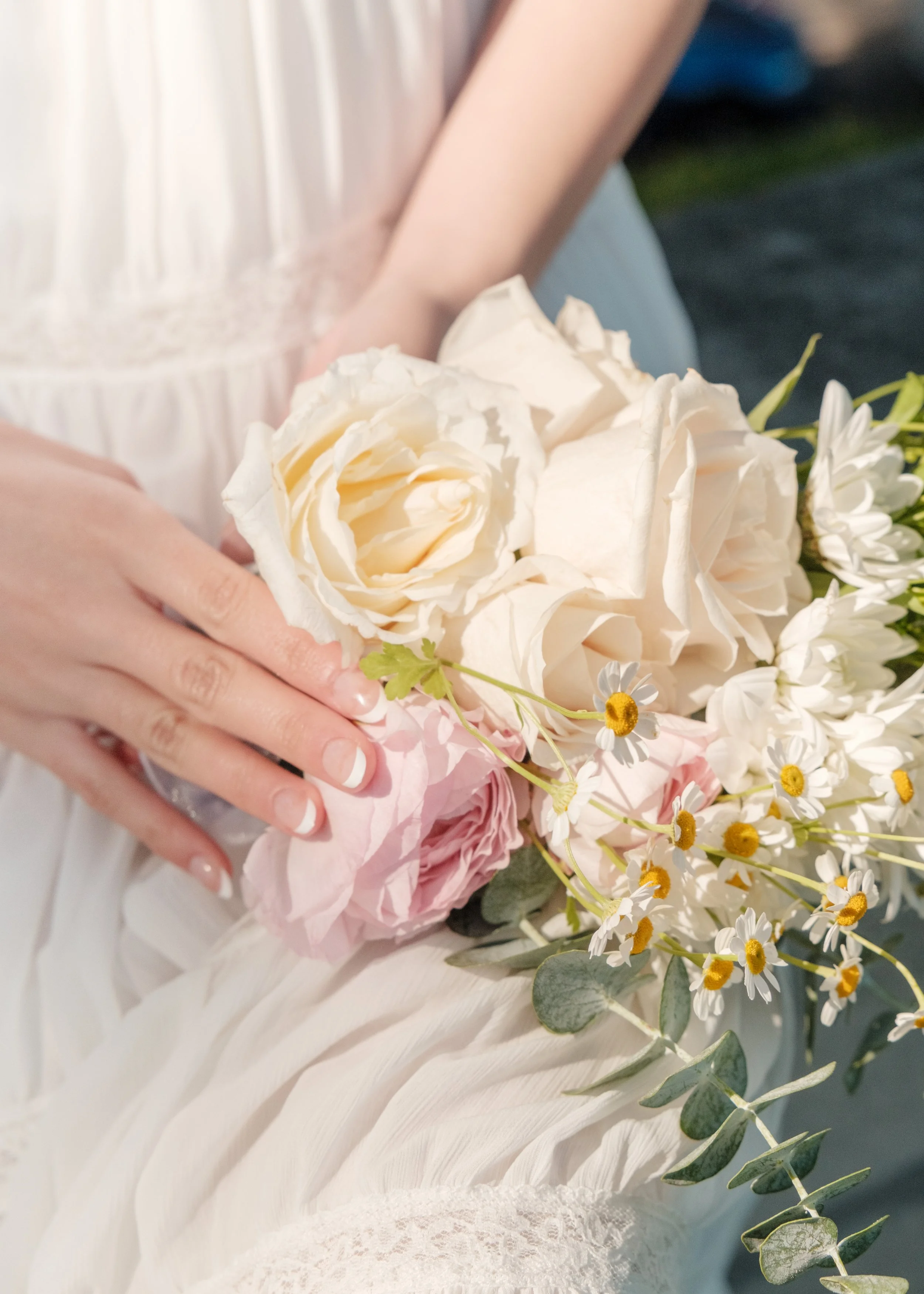 A person in a white dress holding a bouquet of white, pink, and yellow flowers, including roses and daisies.