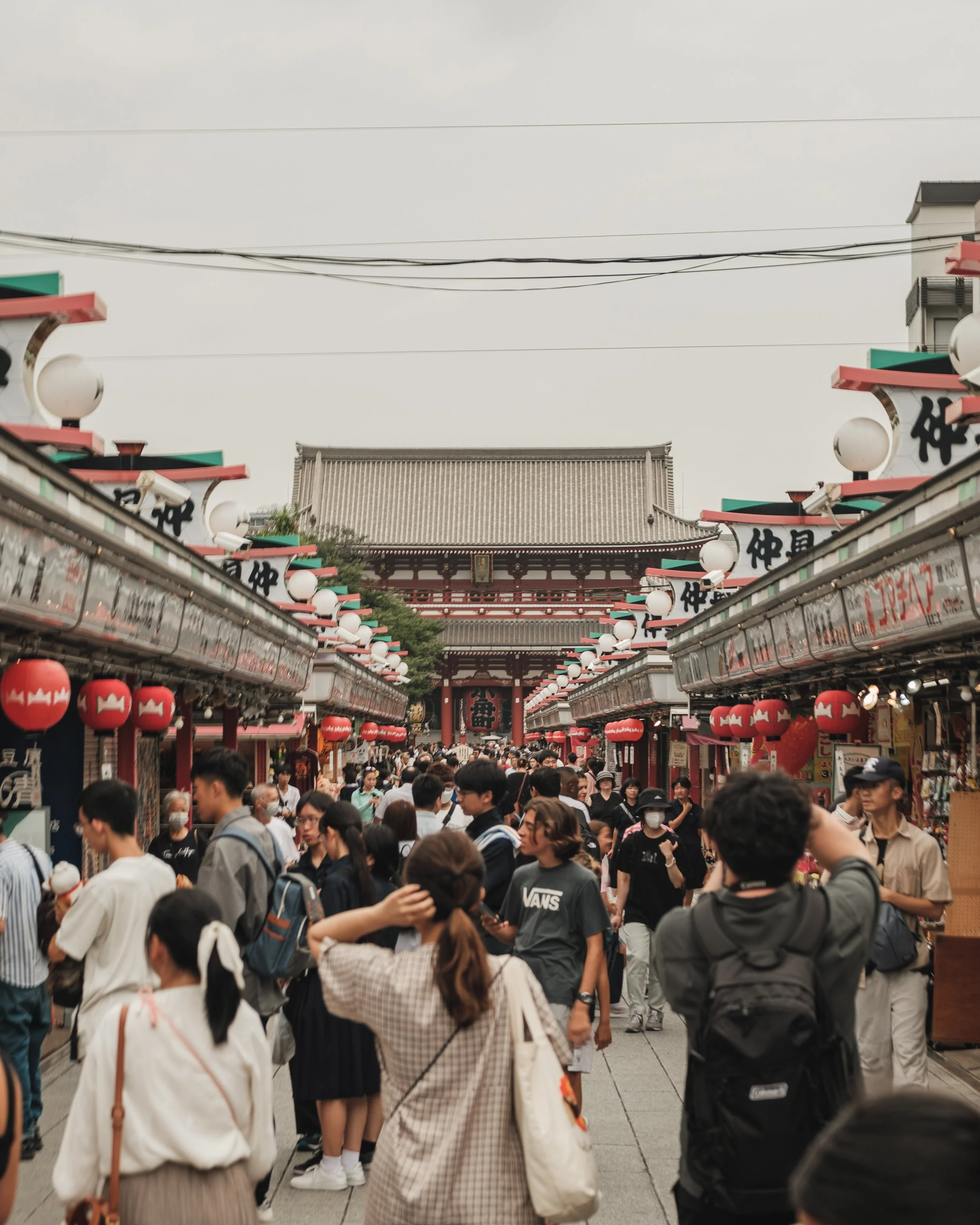 Crowded street market in Japan with traditional red lanterns and a large temple gate in the background.