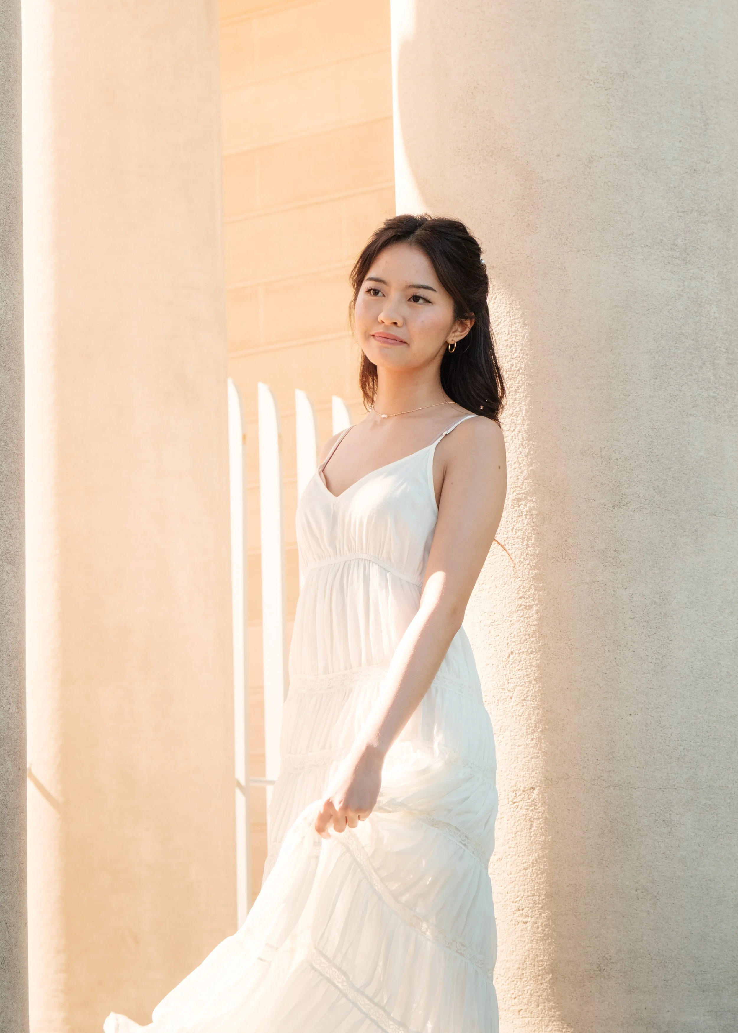 A young woman in a white dress standing outdoors near beige columns