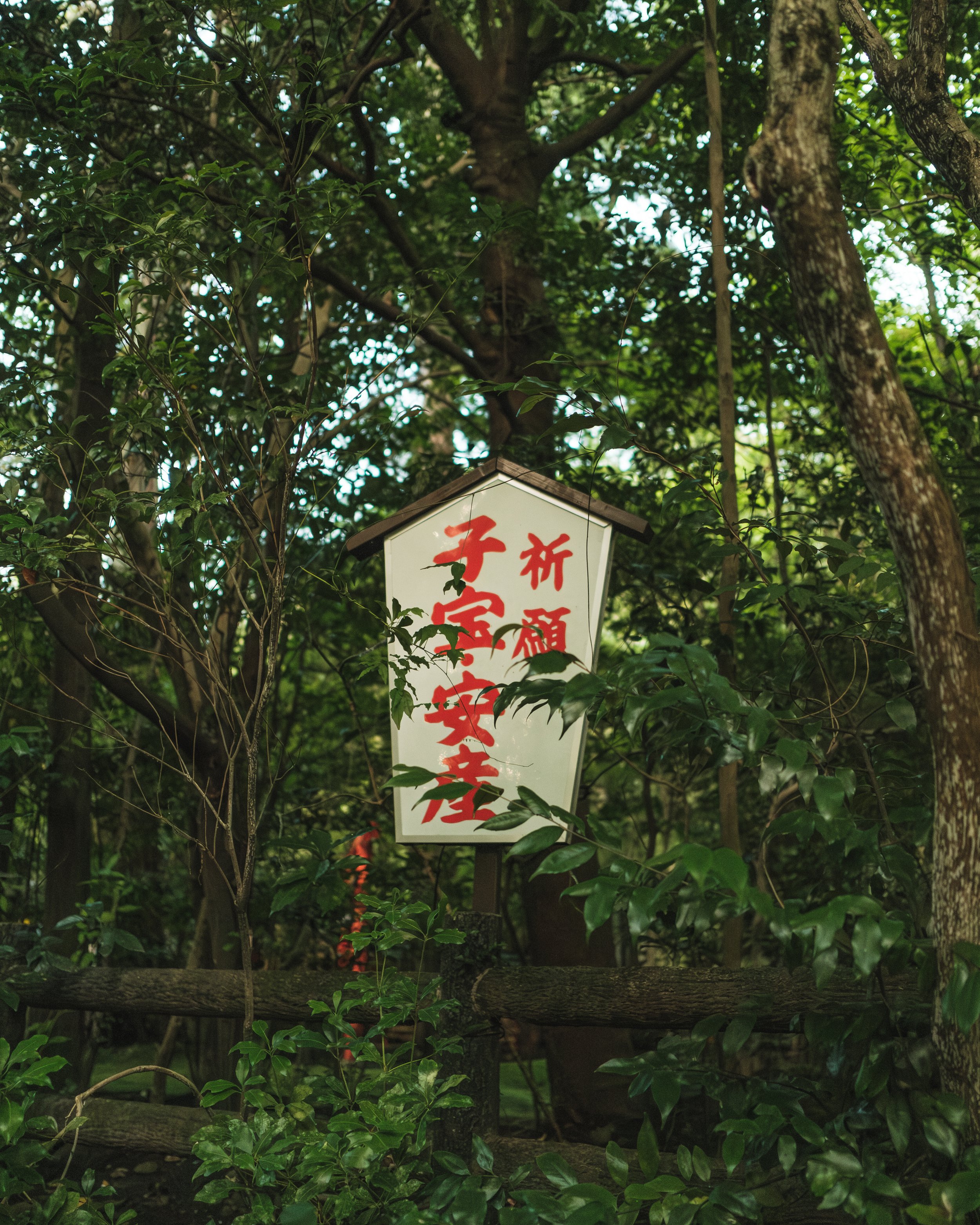 A white, pagoda-shaped sign with red Japanese characters, surrounded by dense green foliage and trees.