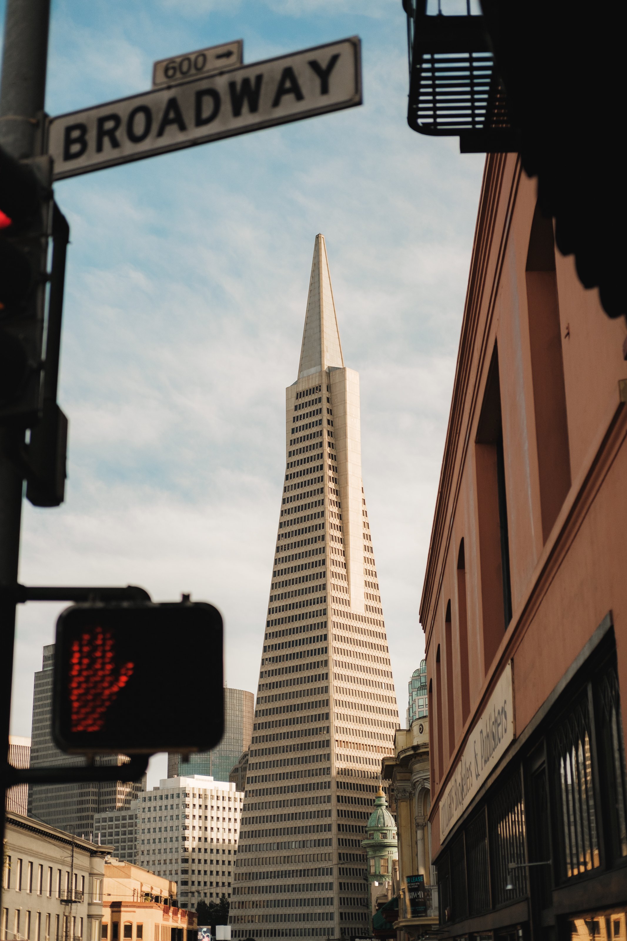 The San Francisco skyline featuring the Salesforce Tower, viewed from a street corner with a Broadway street sign and traffic signals in the foreground.