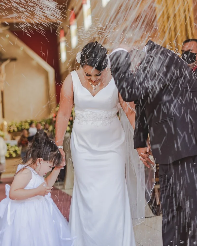 Bride and groom with a young girl at their wedding, surrounded by celebratory sparklers, in a decorated indoor venue.