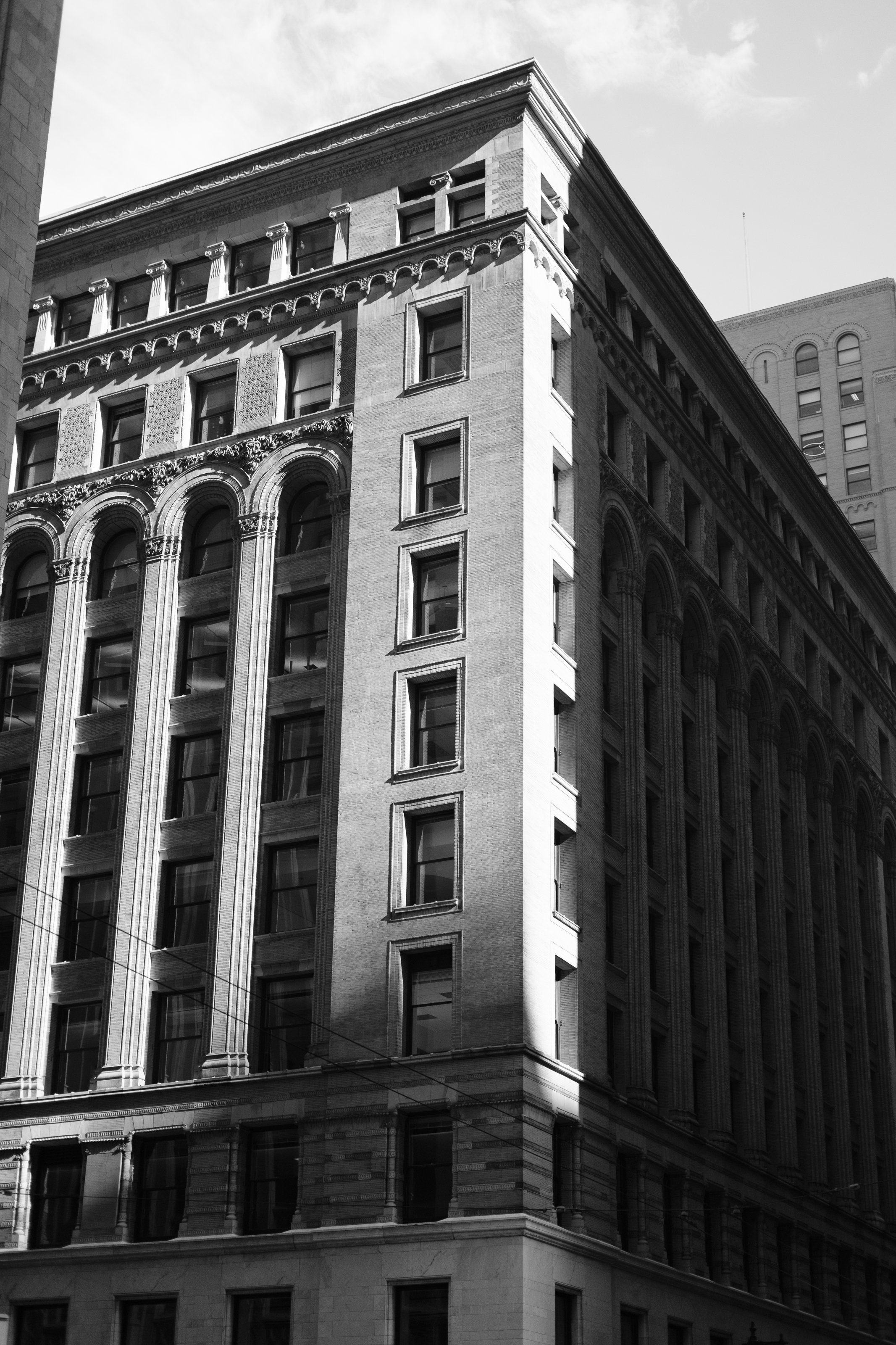 Black and white photograph of a tall, historic building with ornate architectural details, multiple windows, and decorative arches.
