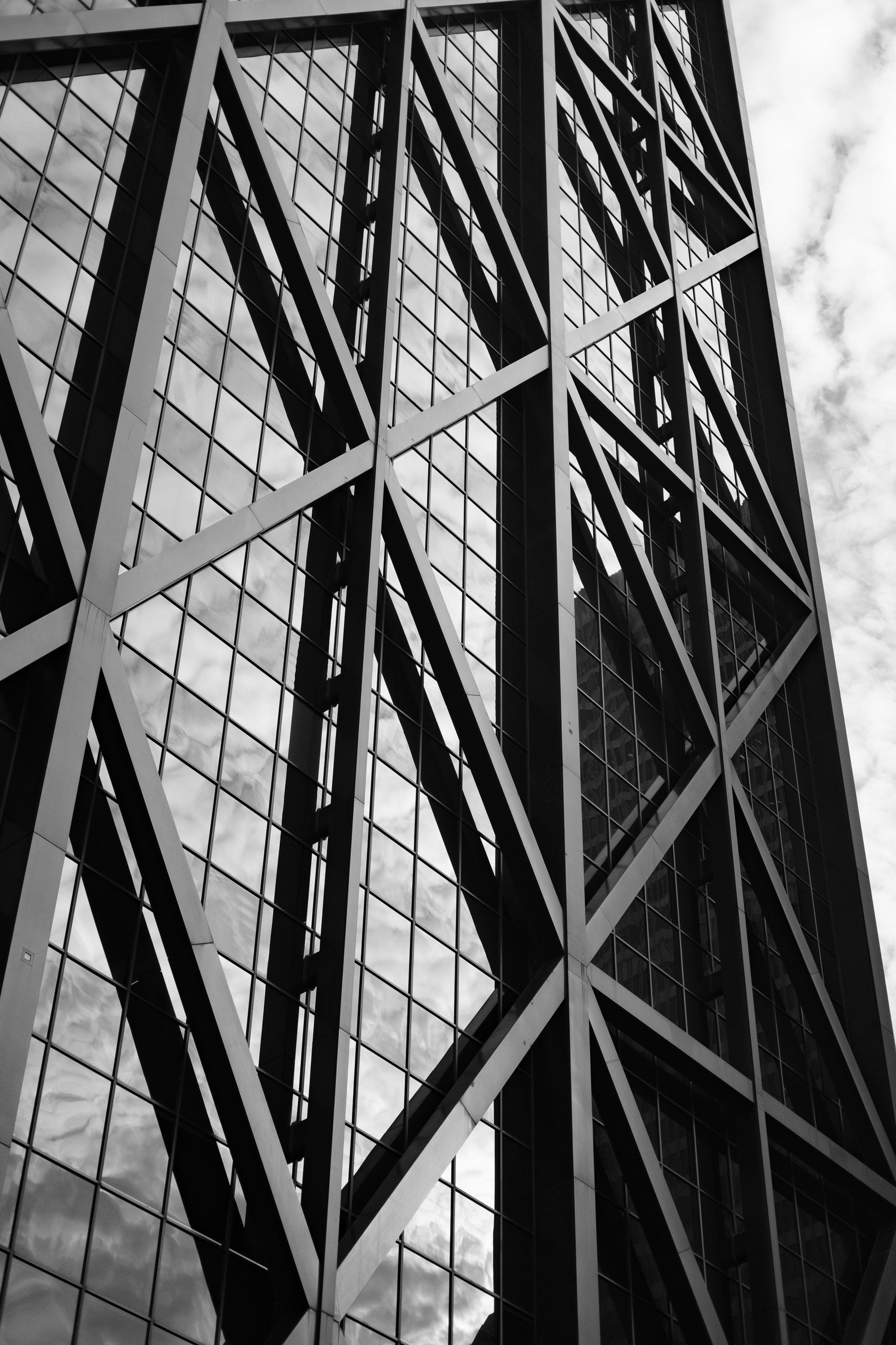 A modern high-rise building with an intricate geometric metal framework and glass windows reflecting clouds in the sky.