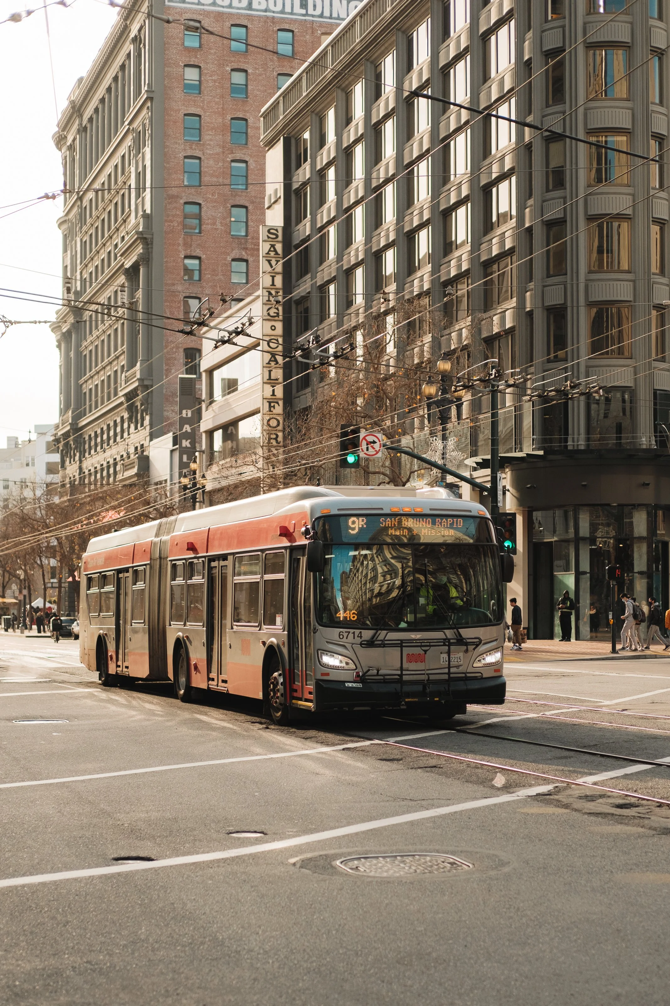 City street scene with a trolley bus on the tracks, surrounded by tall office buildings, pedestrians, and traffic lights.