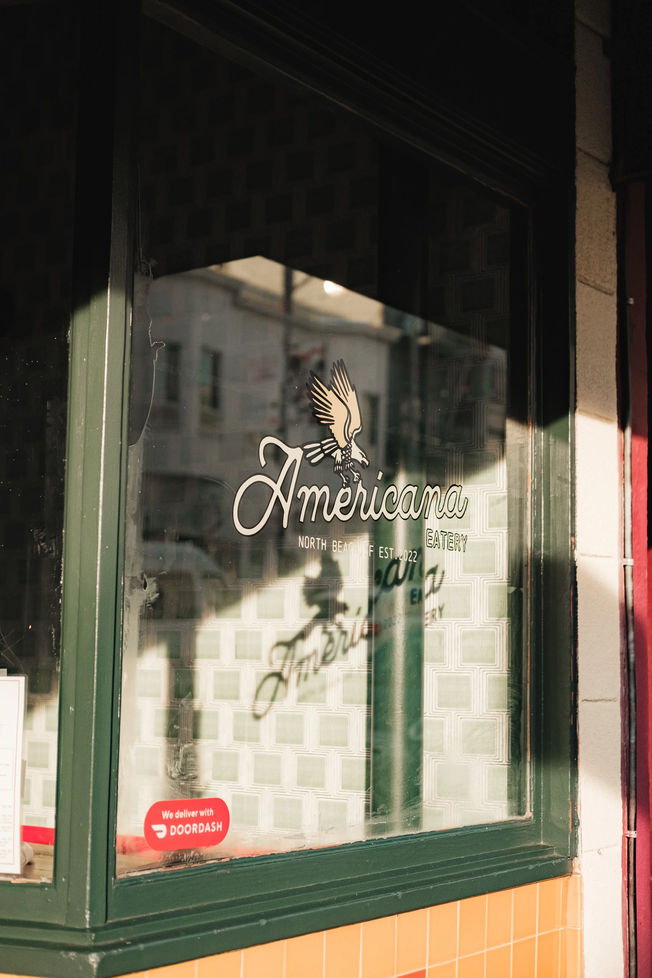 Restaurant window with name 'Americana', featuring a logo of an American eagle, located in North Beach, established in 2022, offering eatery and delivery through DoorDash.
