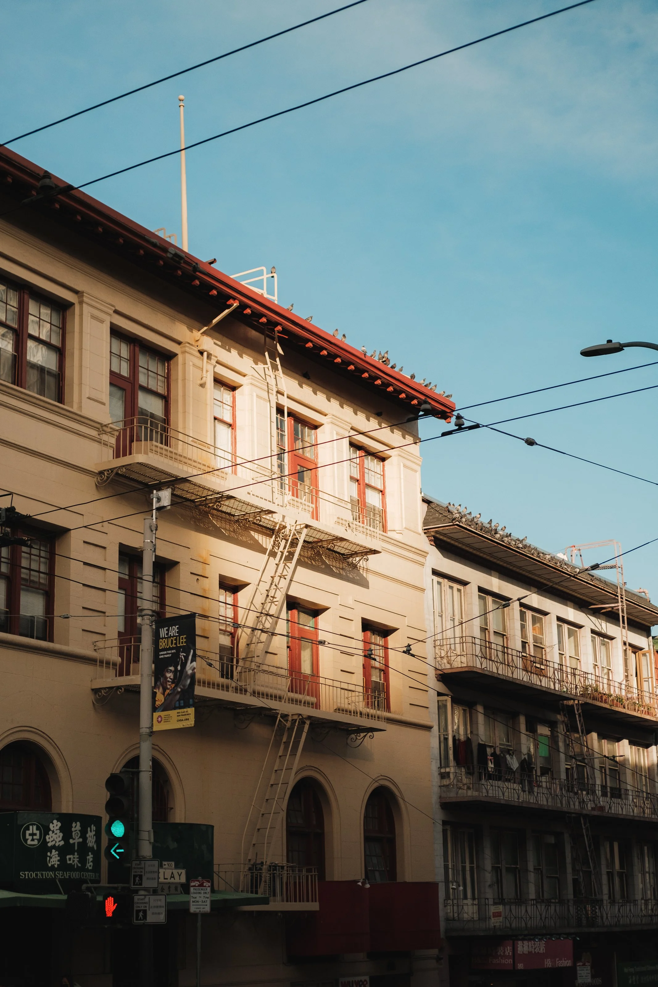 Four-story building with fire escapes and laundry hanging on balconies, above a street with traffic signals and signs, under a blue sky.