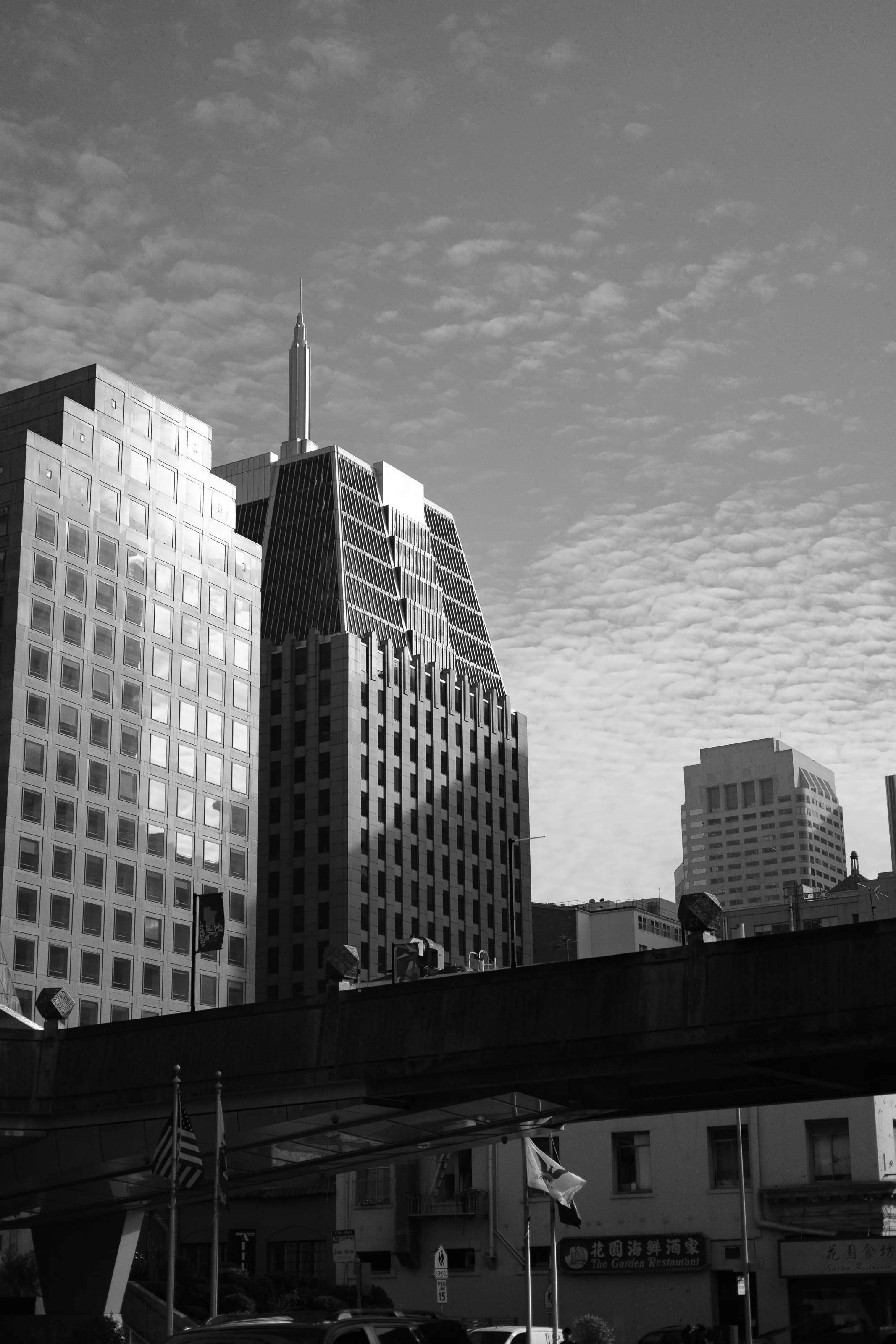 Black and white photo of tall skyscrapers in a city, with a partly cloudy sky above.