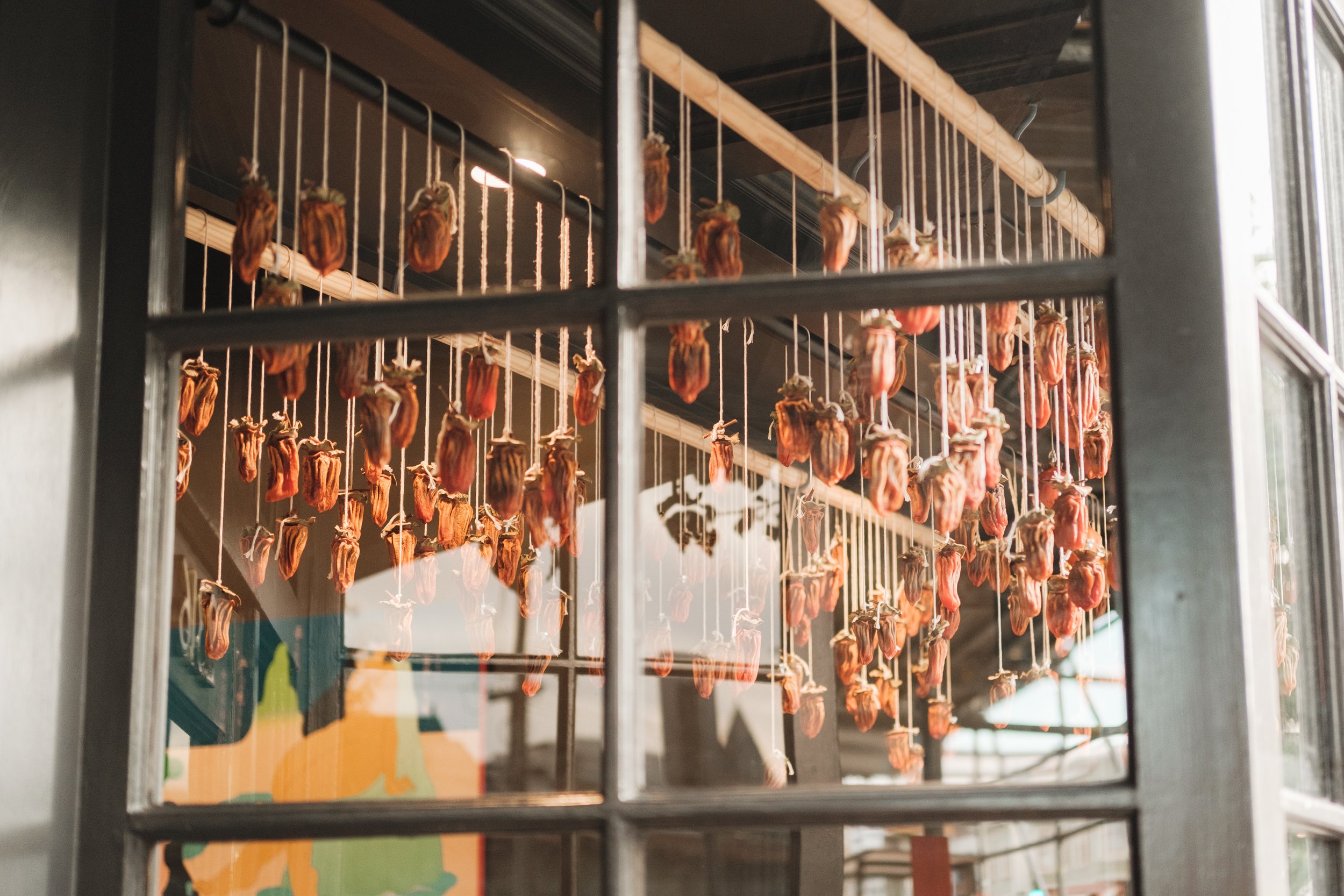 Dried persimmons hanging on strings inside a window display.