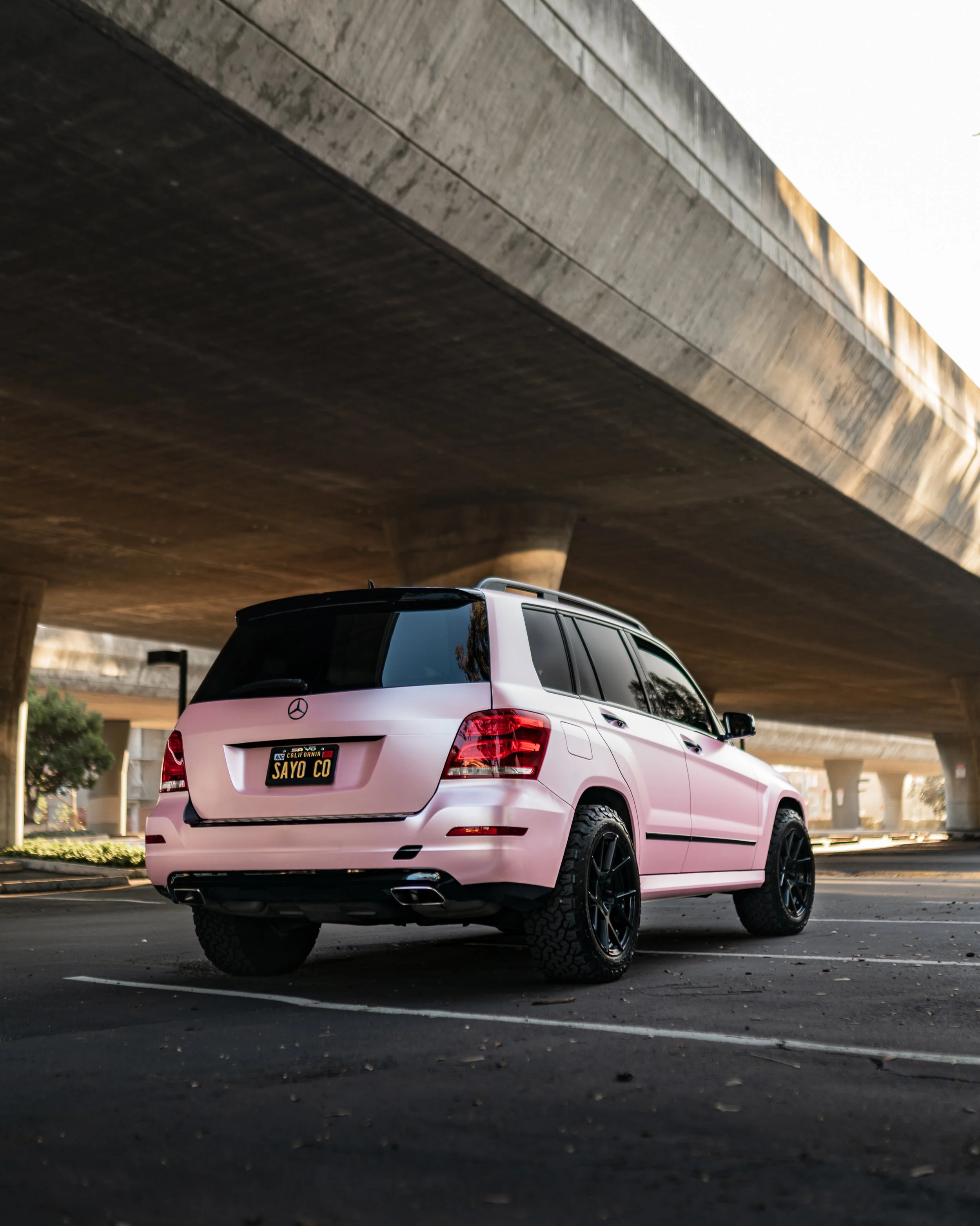 Pink Mercedes-Benz SUV parked under a bridge with a California license plate reading "SAYO CO".