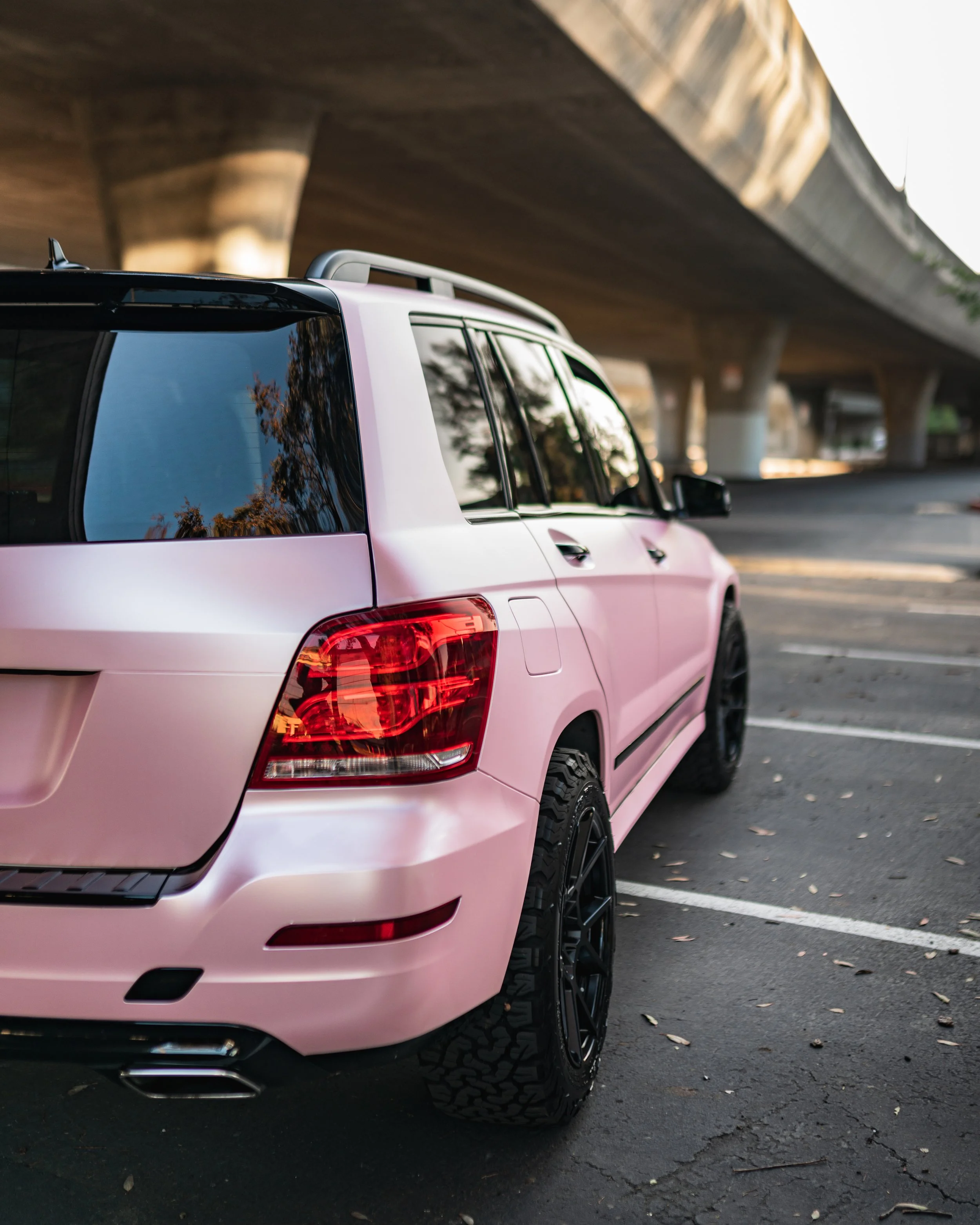 A pink SUV parked under an overpass on a paved lot with white parking lines.