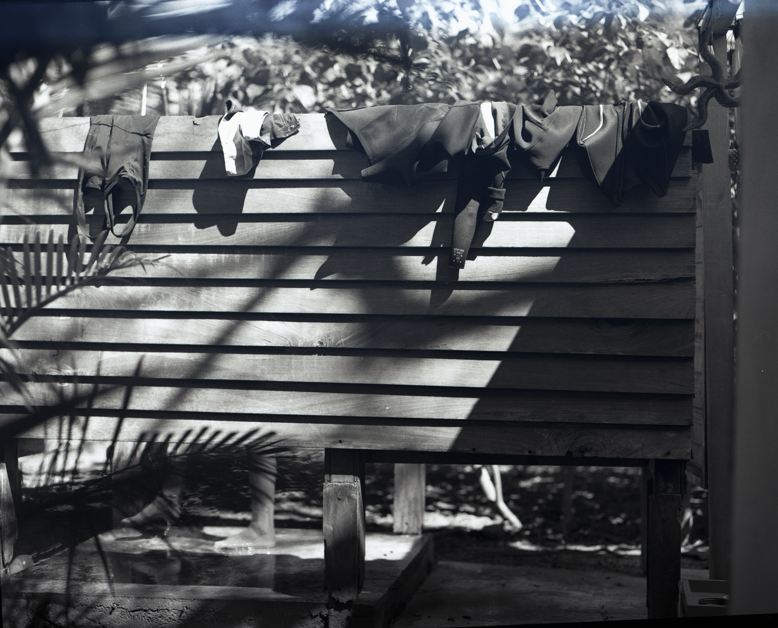 Clothes hanging on a clothesline outdoors with shadows cast on a wooden fence.