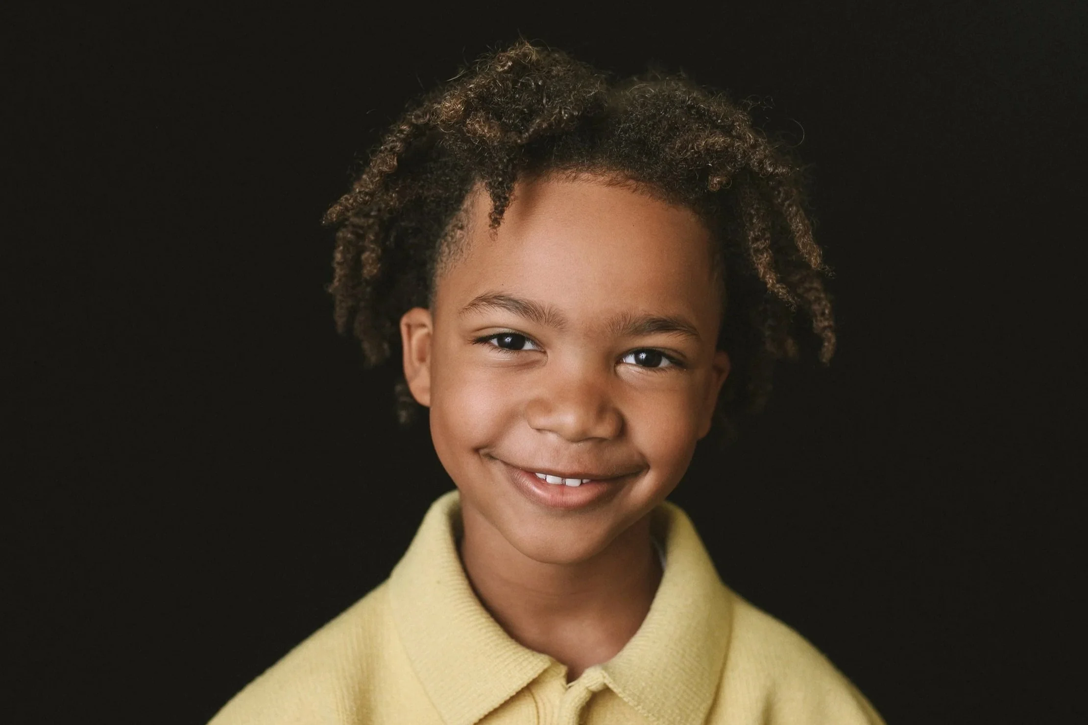 portrait of an elementary school boy with dark skin wearing a light yellow shirt