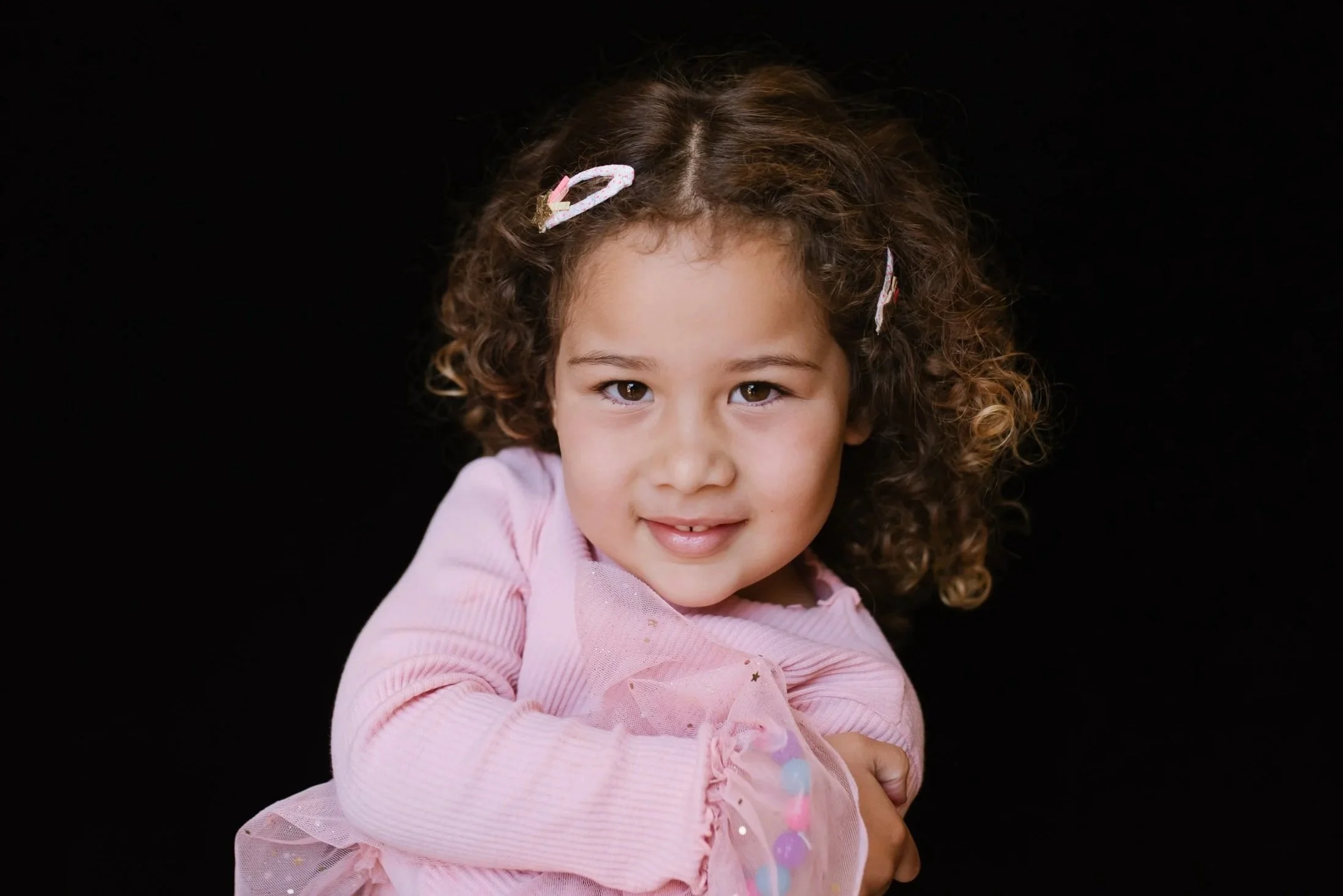Preschool portrait of child in pink sweater on black backdrop.