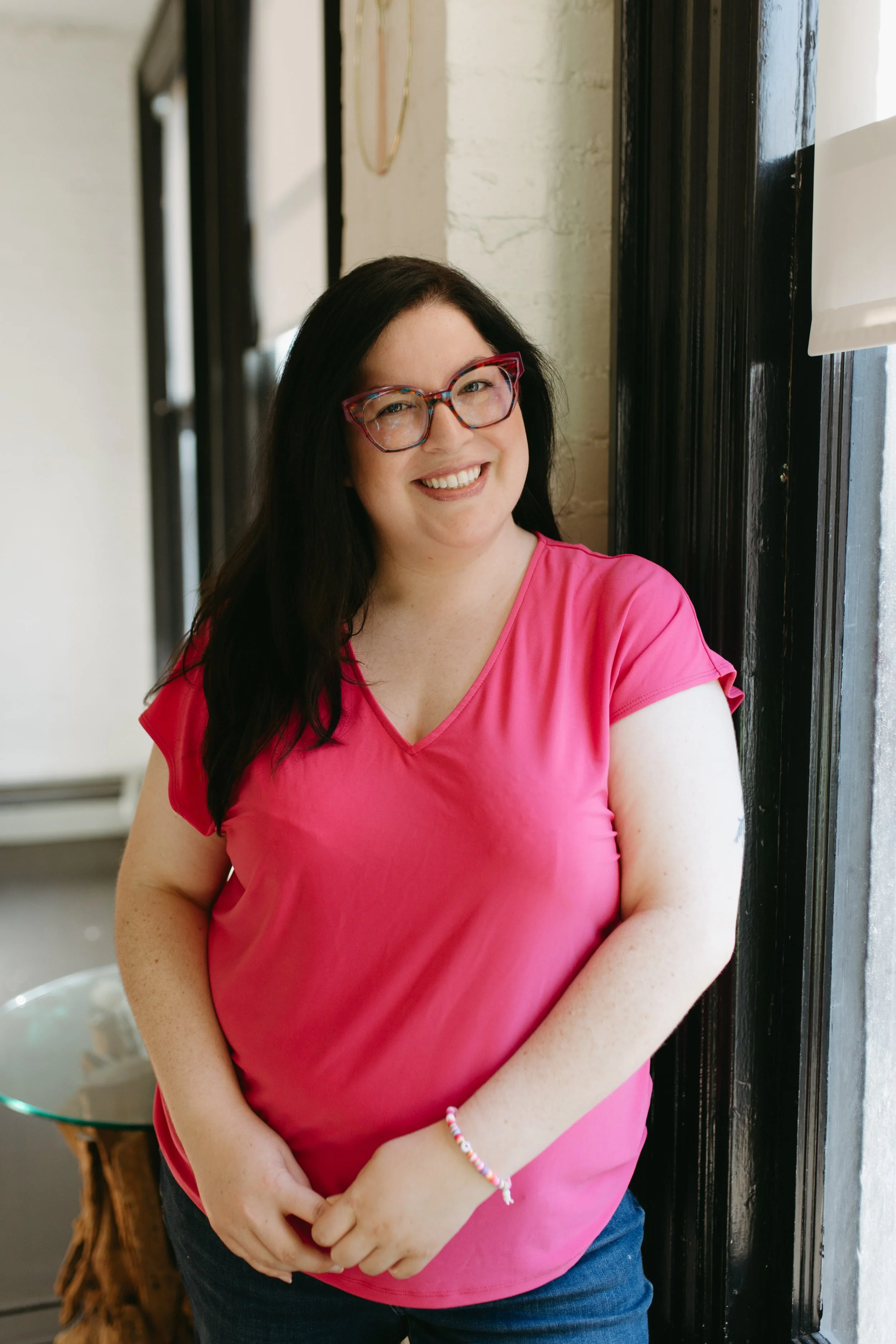 Angelica De Anda standing calmly by a window smiling. Providing EMDR therapy session for anxiety, burnout, and trauma recovery in Kirkland, Washington.