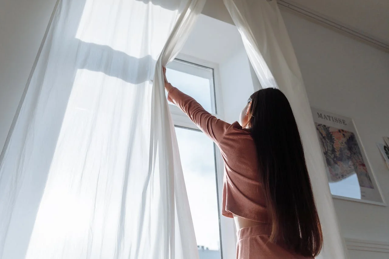 Woman opening curtains to let in morning light, symbolizing gentle New Year intentions, mental health goals, and emotional well-being