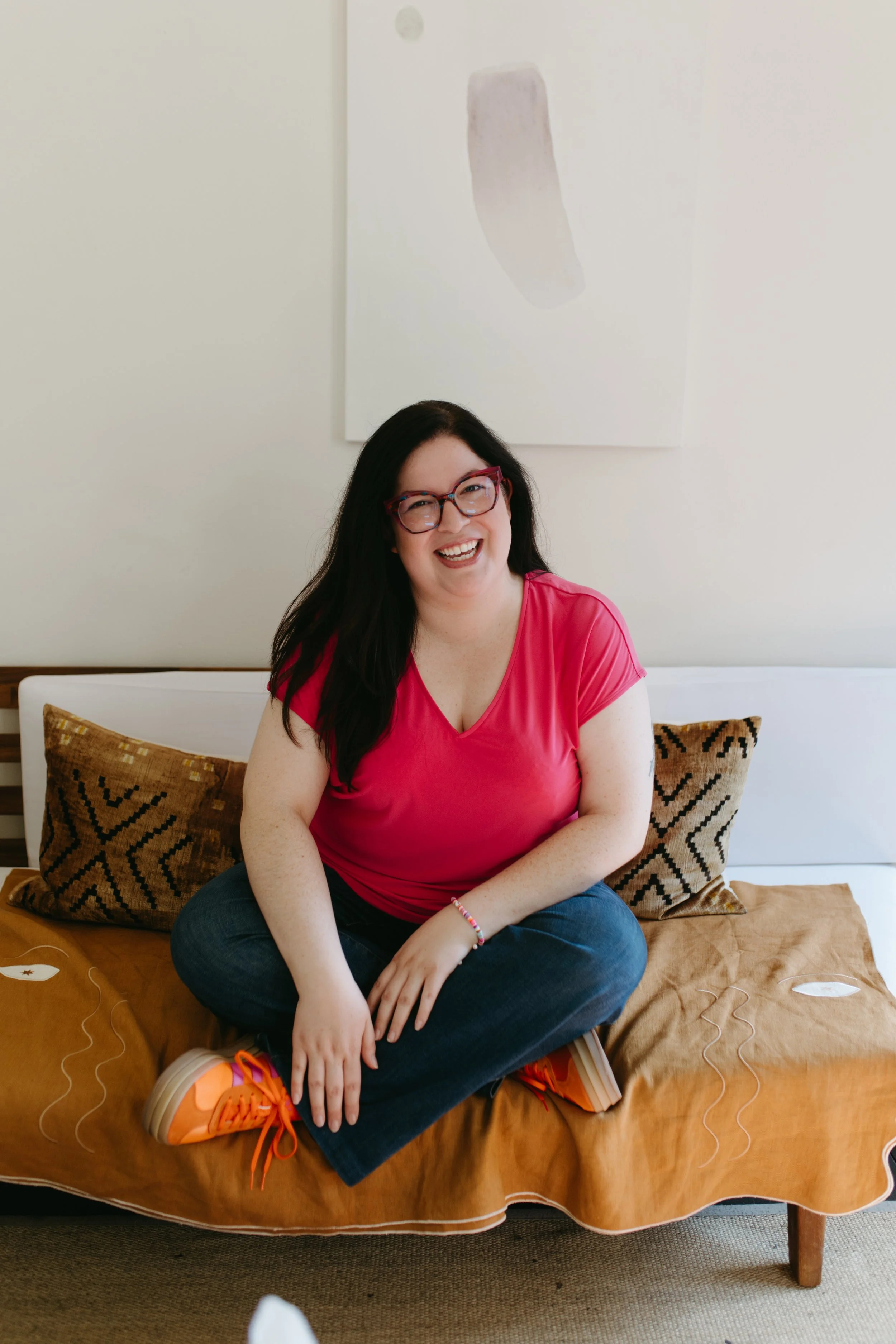 Angelica De Anda smiling warmly while seated on a couch, creating a welcoming space for EMDR therapy, trauma healing, and anxiety support in Kirkland, Washington.