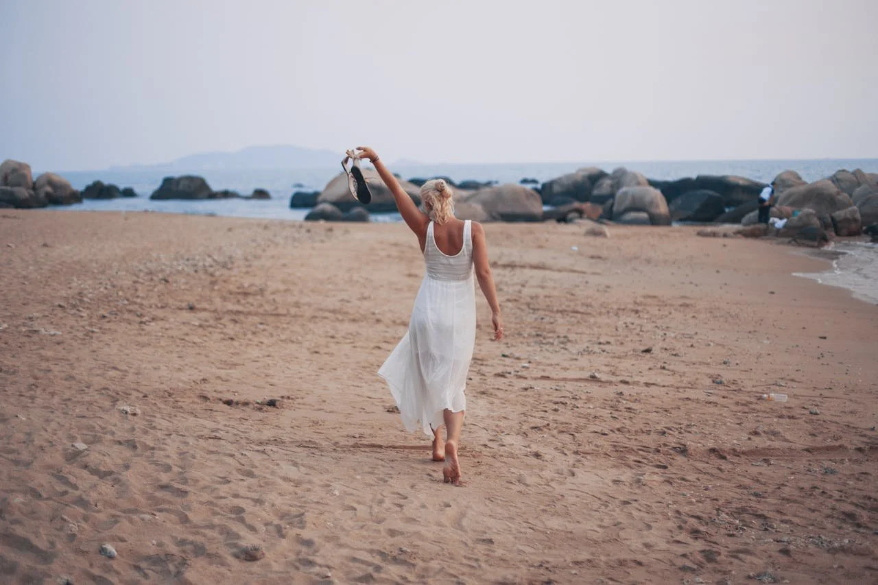 Woman walking barefoot along the beach, symbolizing forward momentum and emotional relief that can come from investing in mental health through focused therapy support and therapy intensives.