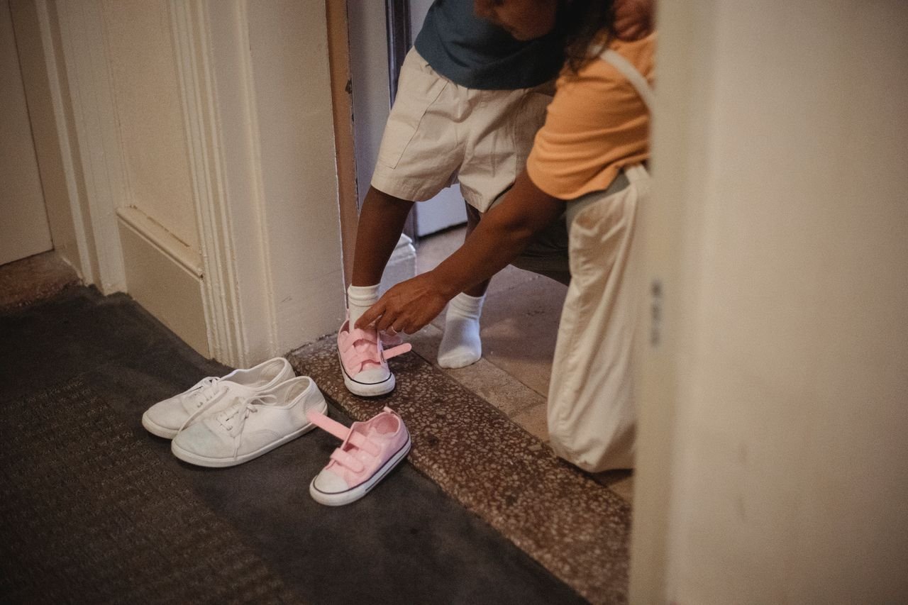 Parent kneeling to help child put on shoes during a rushed back to school morning, reflecting parent anxiety and nervous system activation