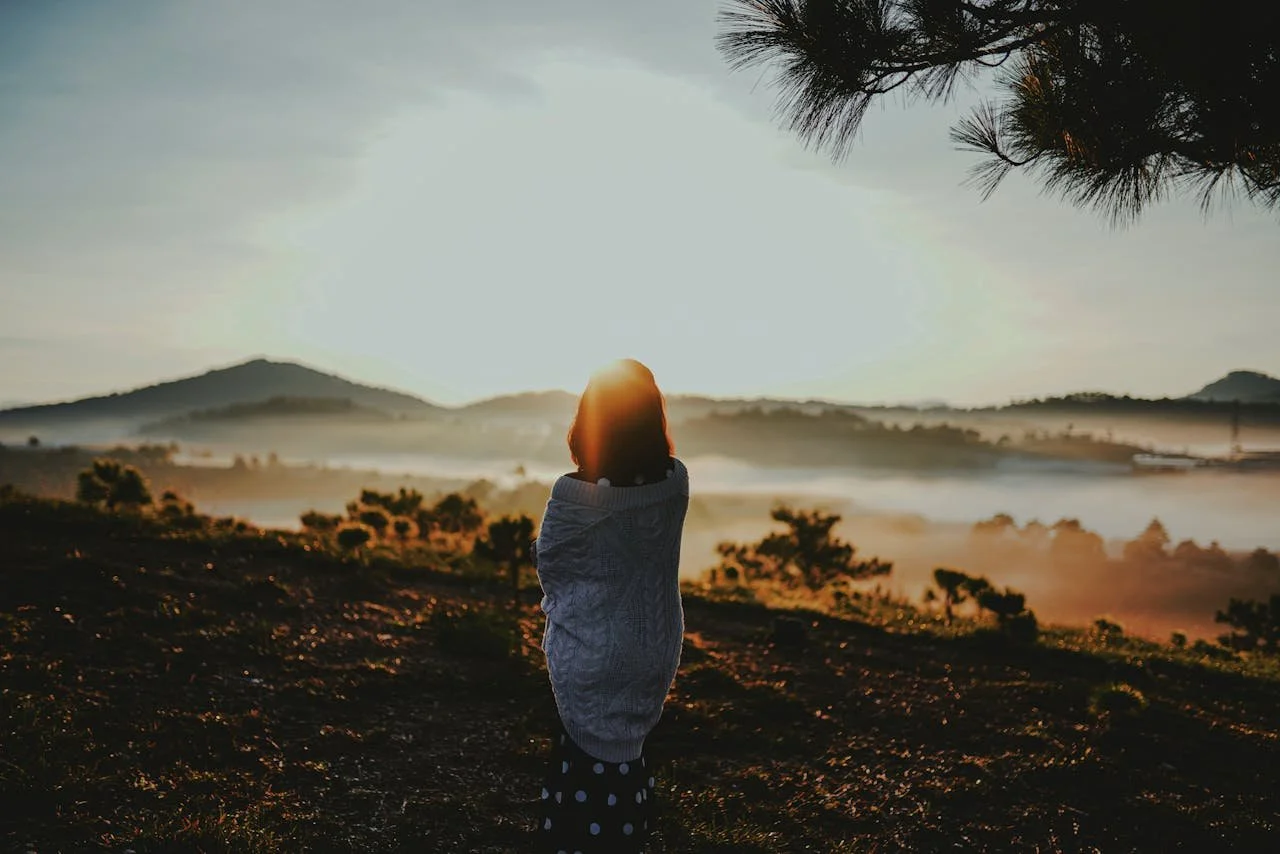 Woman standing in nature at sunrise, reflecting on emotional healing and letting go of the past while preparing to start fresh in the new year.
