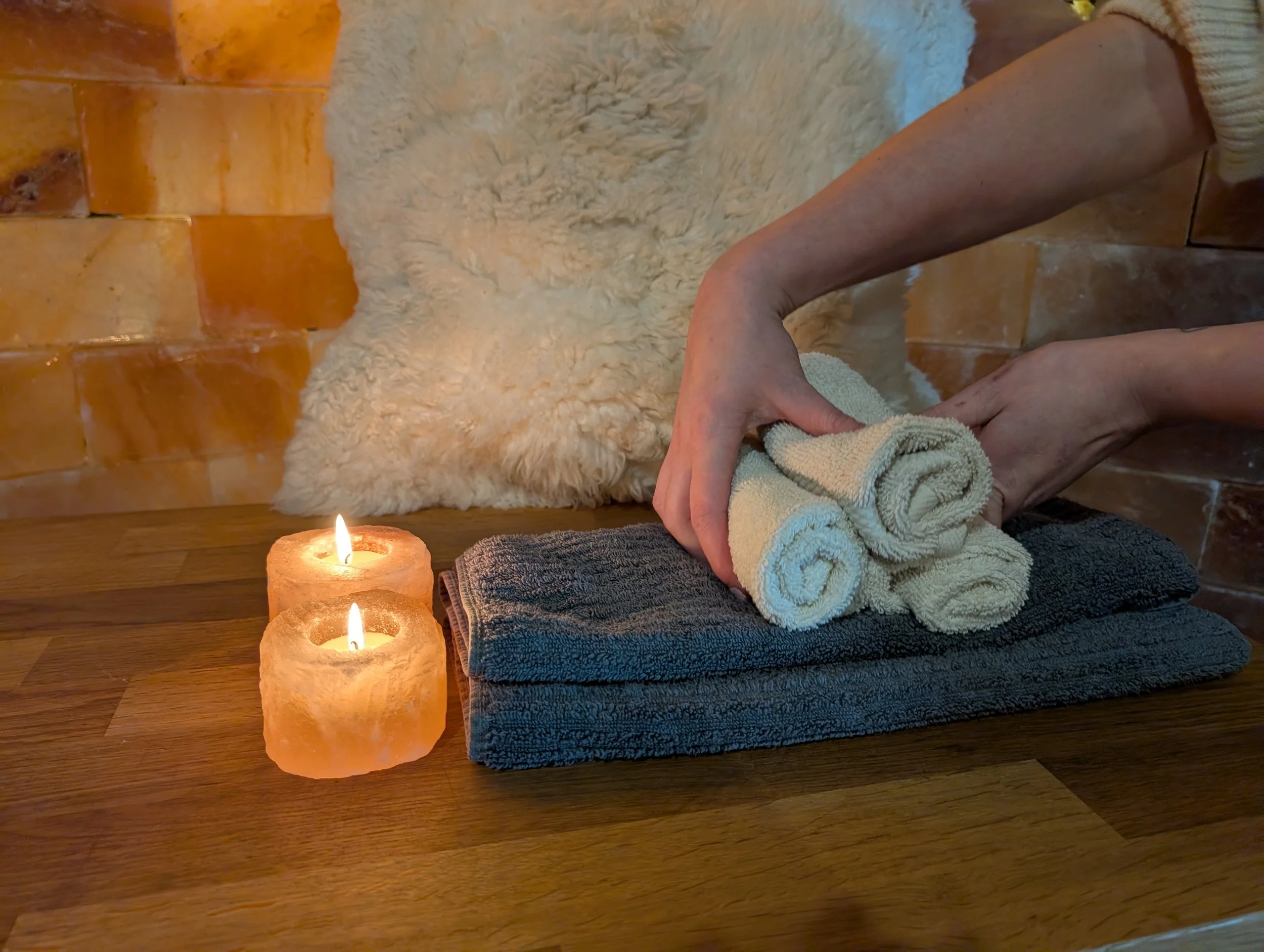 Massage therapist placing towels on a bench beside glowing Himalayan salt votives.