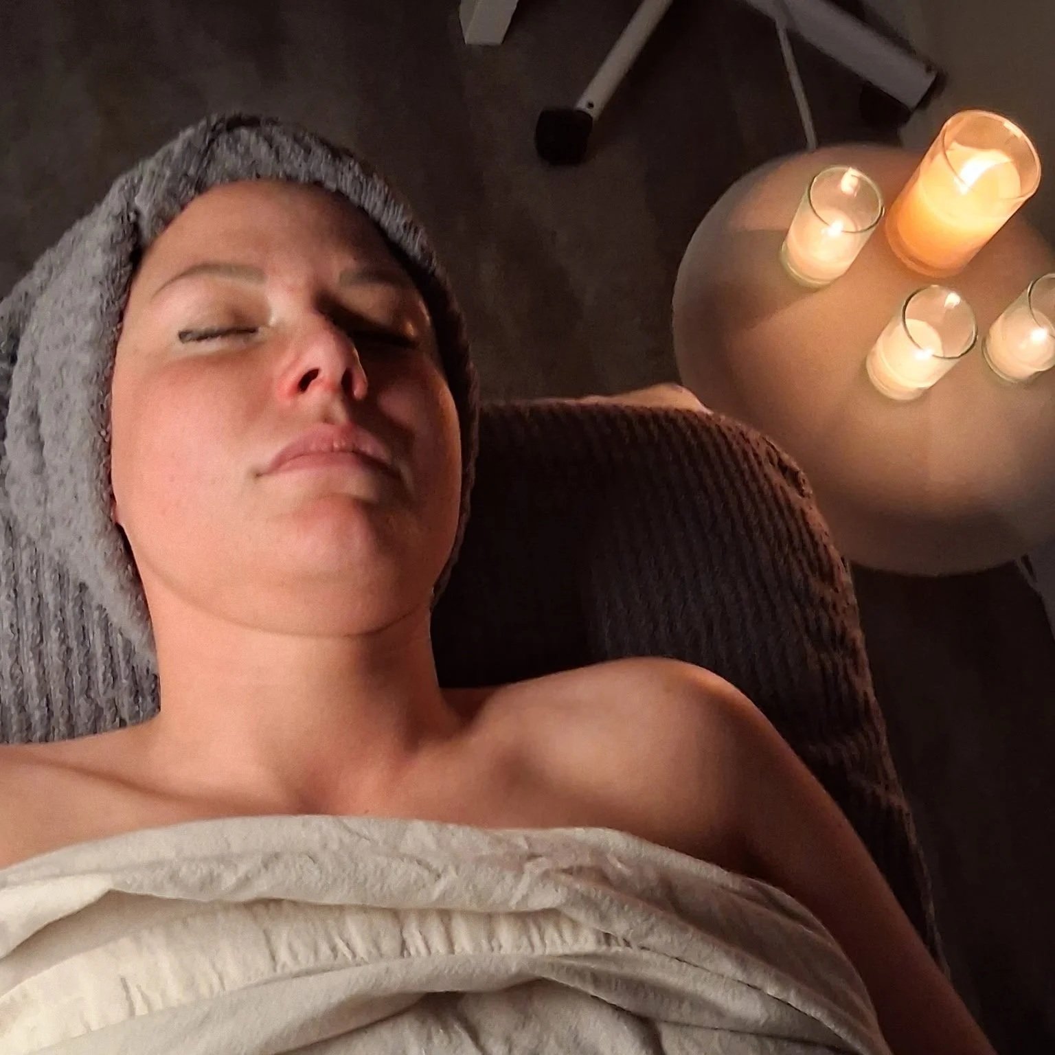 Woman relaxing on an aesthetic bed ready for her Sæla Facial with candles in the background.
