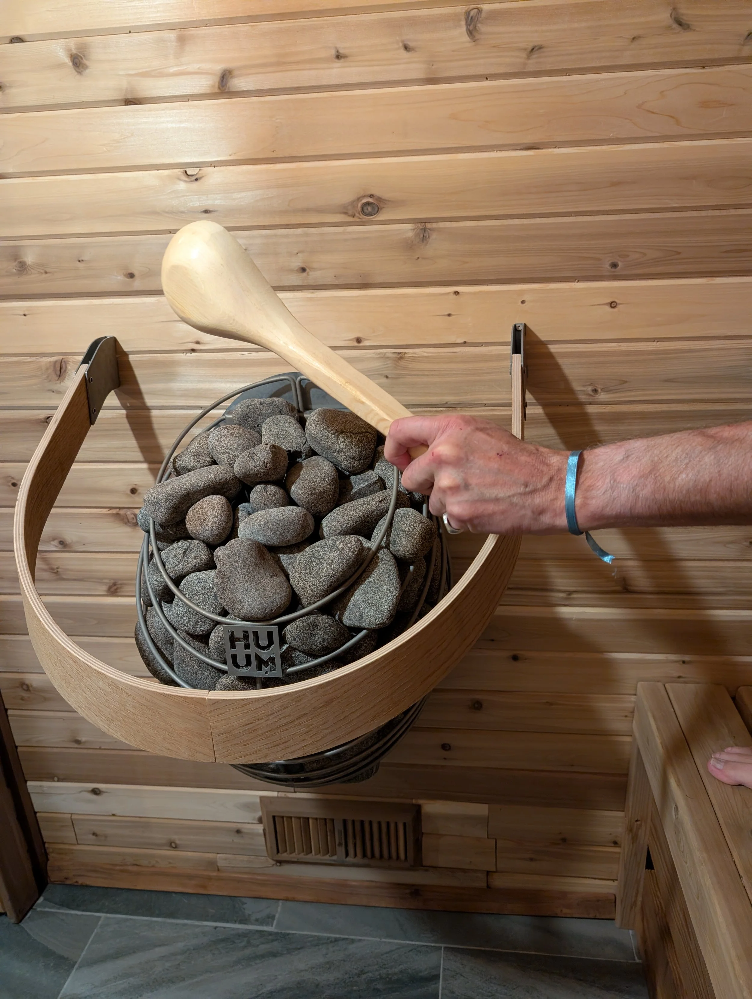 Man pouring water over hot rocks on Huum stove in Finnish sauna 