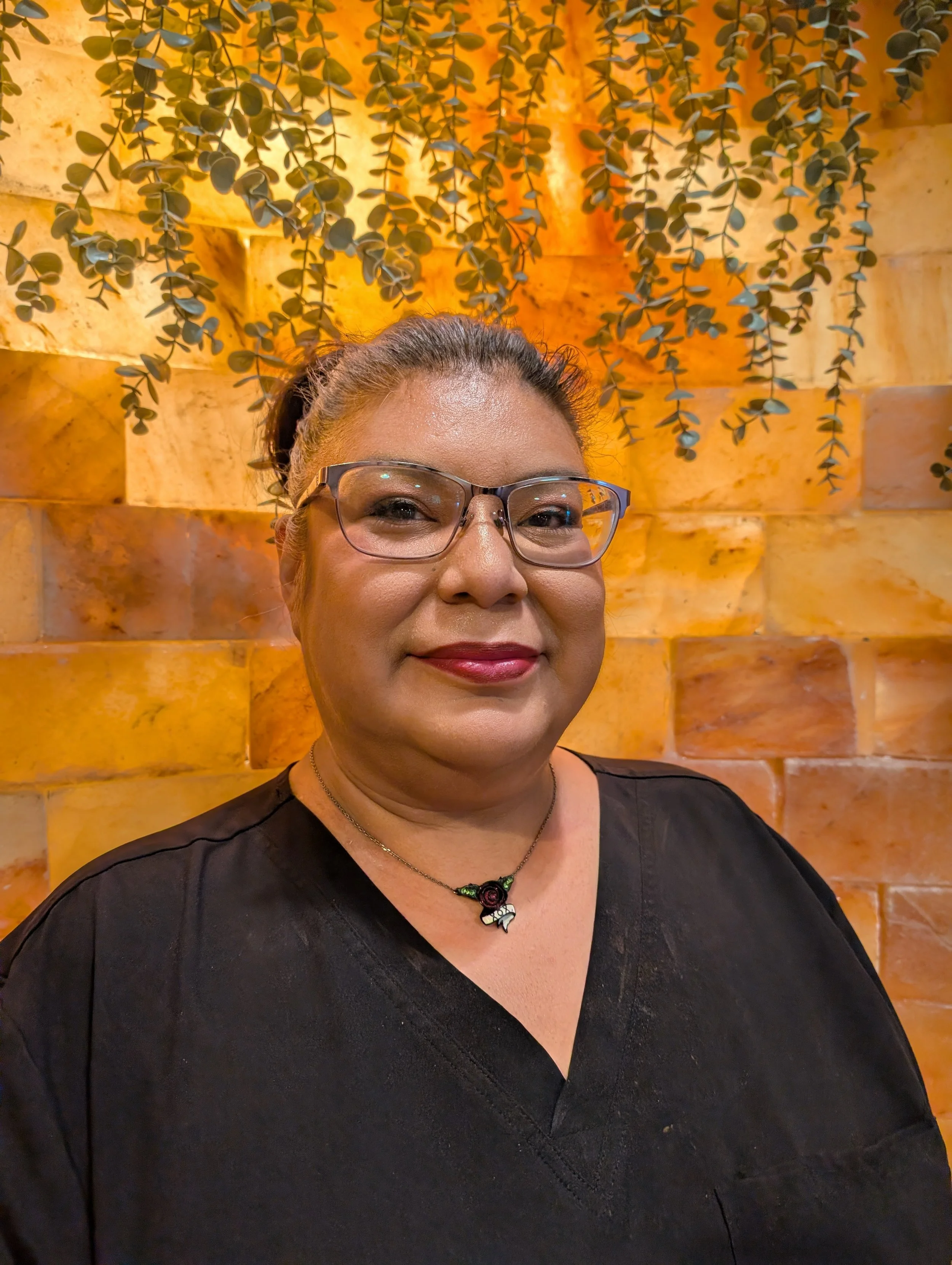 Portrait of a woman with short black hair, wearing a black top, standing in front of a wooden textured background.