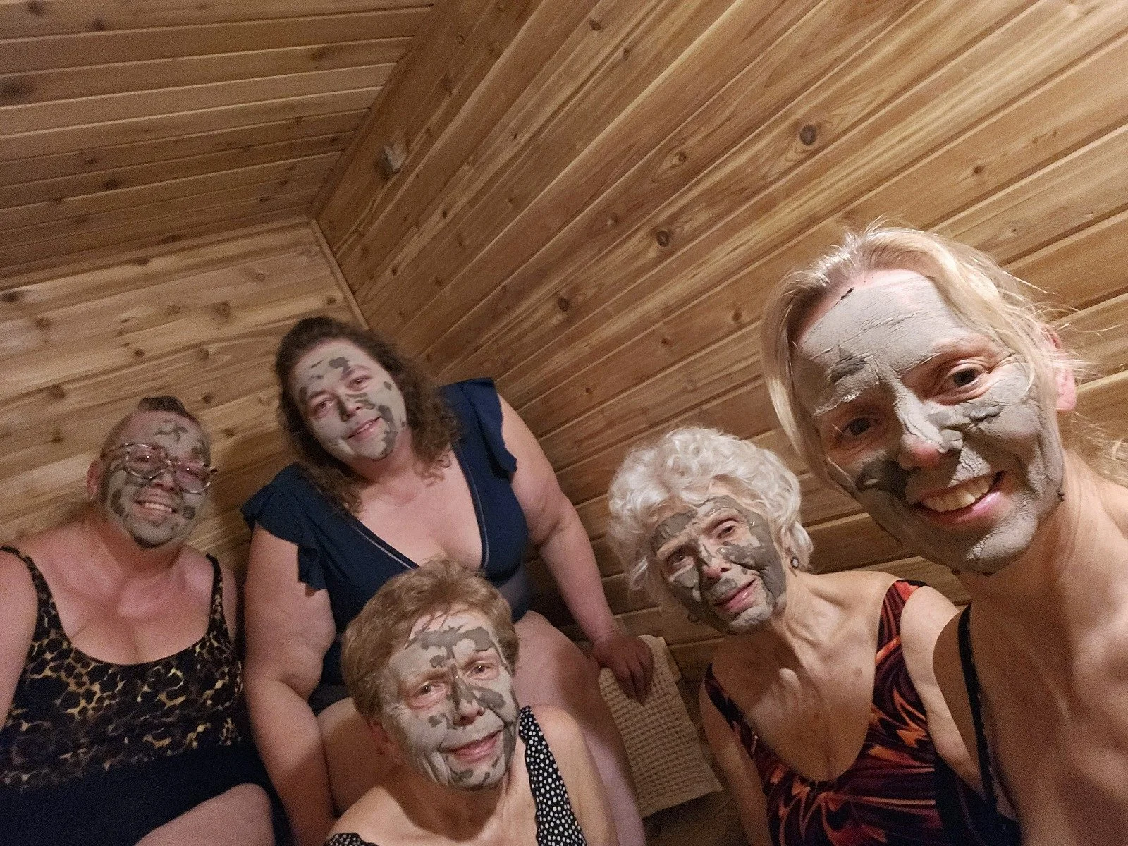 Group of six women with face masks in a wooden room, smiling at the camera.