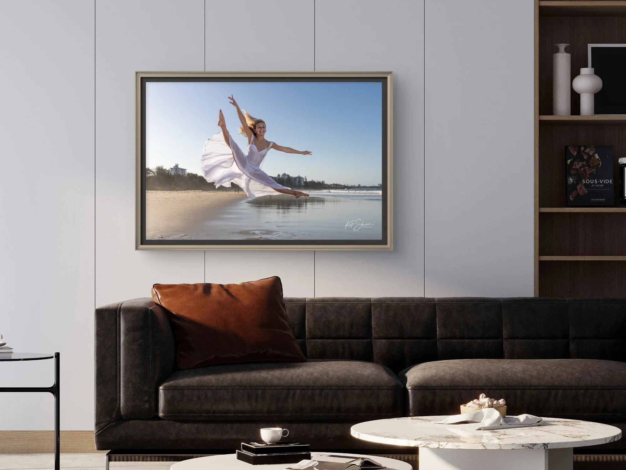 Modern bedroom with dark wood bed, gray bedding, framed abstract art, two indoor plants, and a round table lamp next to the bed.
