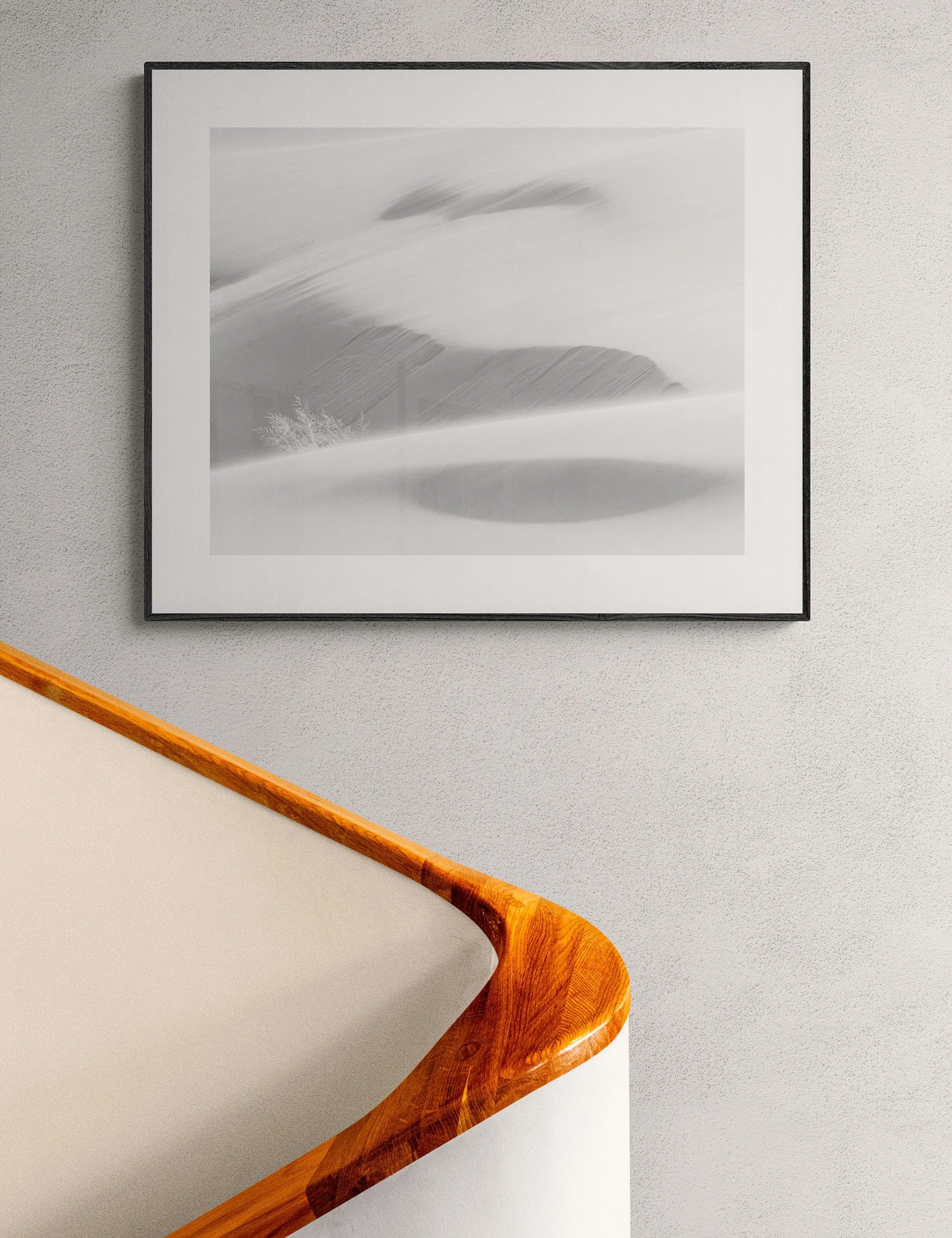 “Dunes of the Dreamworld” framed monochrome landscape print by Ian J. Muirhead Arts above a curved timber staircase in a minimalist interior. Soft abstract dunes and shadows create a dreamlike scene.