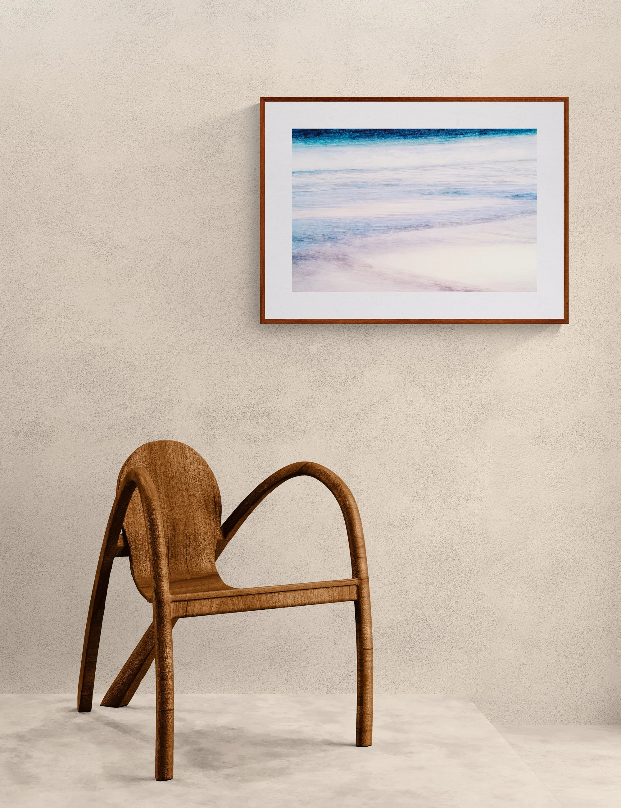 Minimalist coastal fine art print “Serene Swash” displayed in a warm timber frame with white mat on a textured neutral wall above a sculptural wooden chair in a calm contemporary interior.