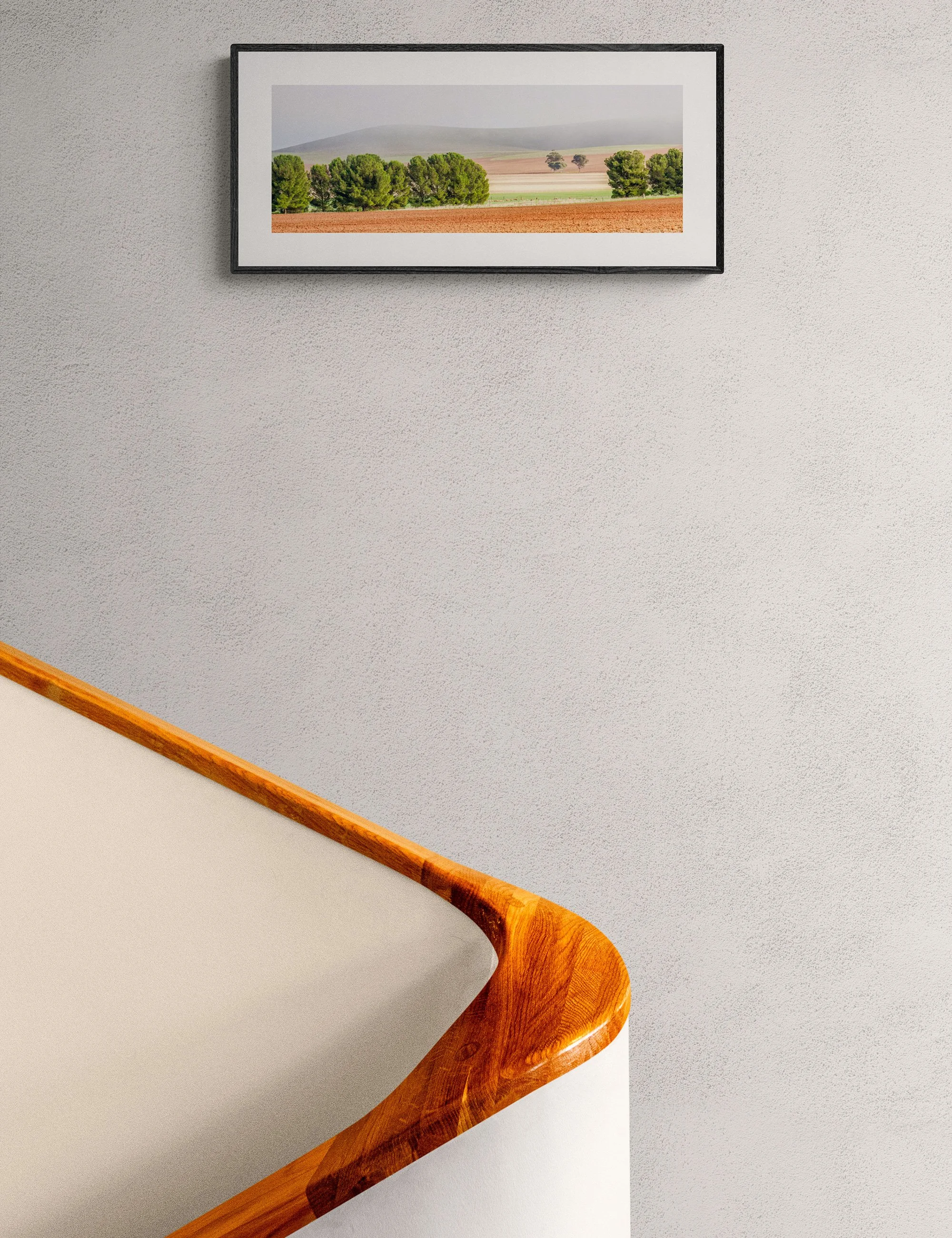 “Rainbow Fog” framed landscape print by Ian J. Muirhead Arts above a curved timber staircase in a minimalist interior.