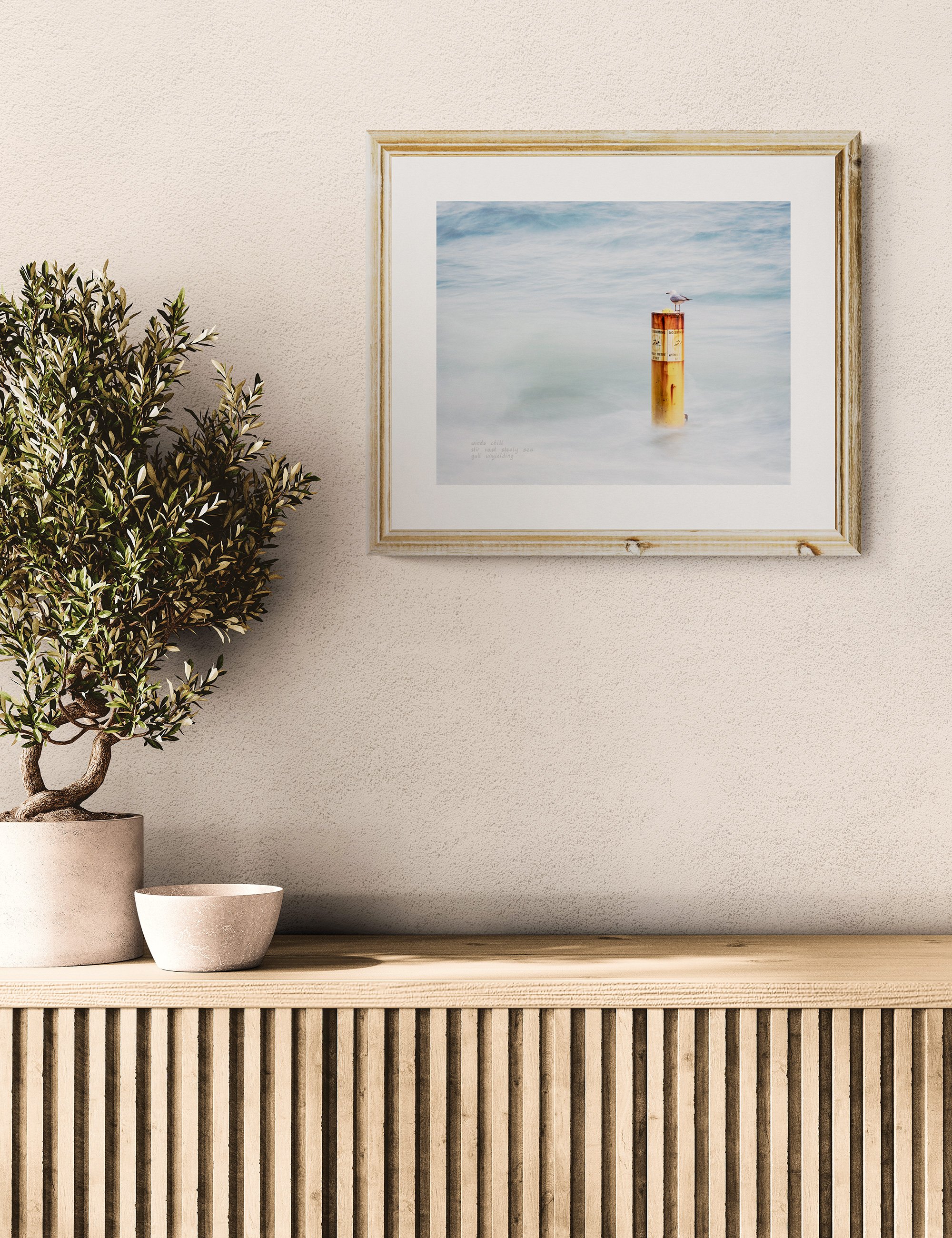 “GULL UNYIELDING” haiga print by Ian J. Muirhead Arts, featuring a lone gull on a sea marker with soft coastal tones and embedded haiku.