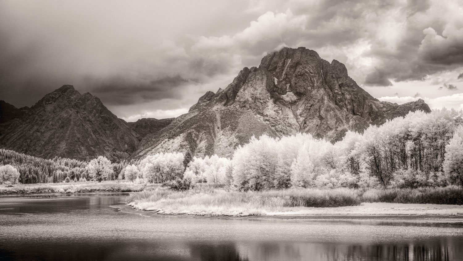 An infrared monochrome photograph of Snake River with cloud-cloaked Tetons in Wyoming.
