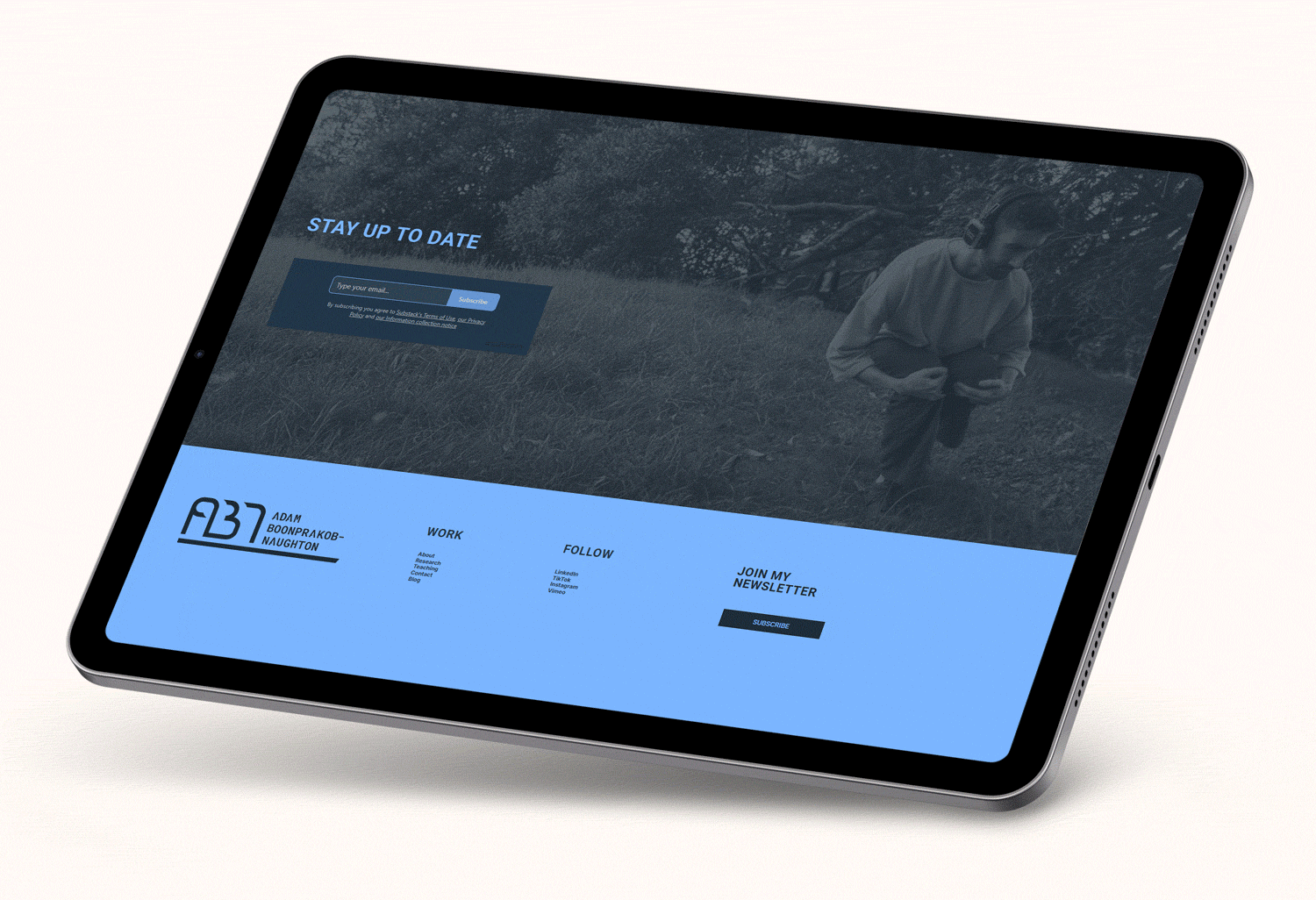Tablet screen displaying a website with a dark photo of a man walking outdoors, a newsletter signup box, and a footer with the name Adam Boonprakob-Naughton and sections for work, follow, and newsletter subscription.