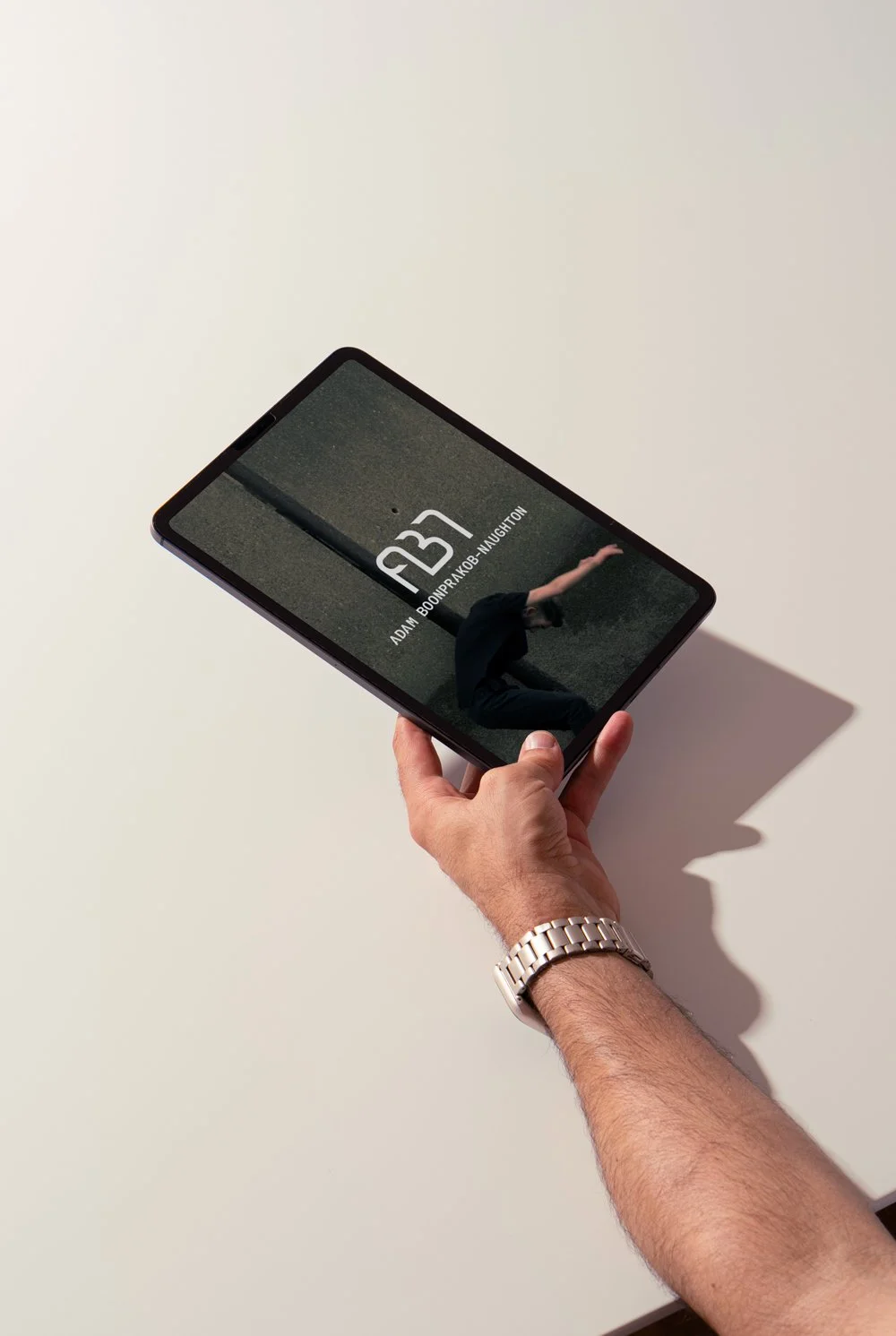 A person holding a tablet with a photo of a person sitting against a concrete wall on the screen.