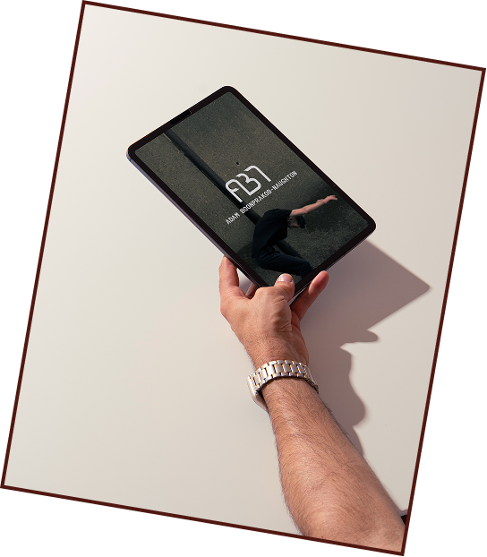A hand holding a tablet with a black cover, displaying the date 'Monday, 1 August' and the time '3:13' on the screen, with a reflection of a person doing a handstand visible on the tablet.